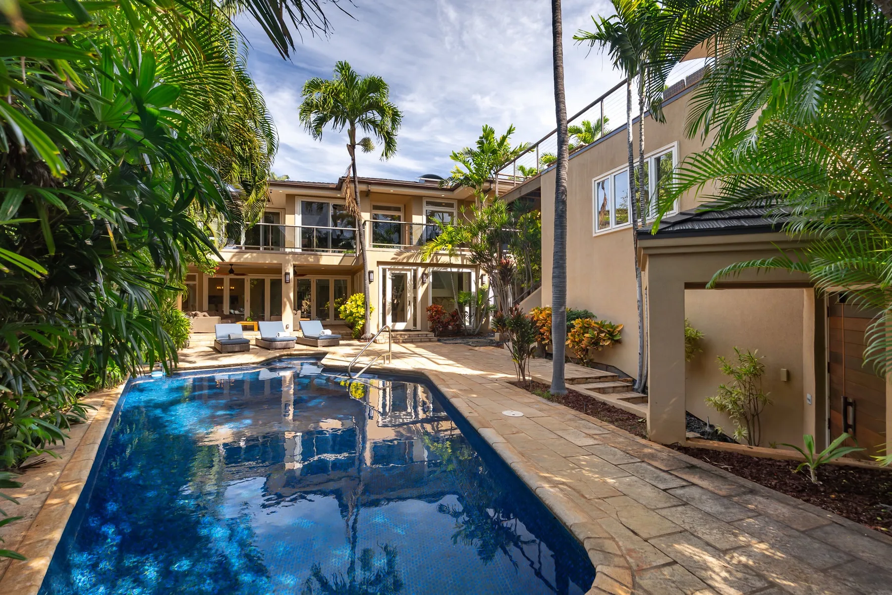 A swimming pool sits beside a paved patio and a multi-story building.