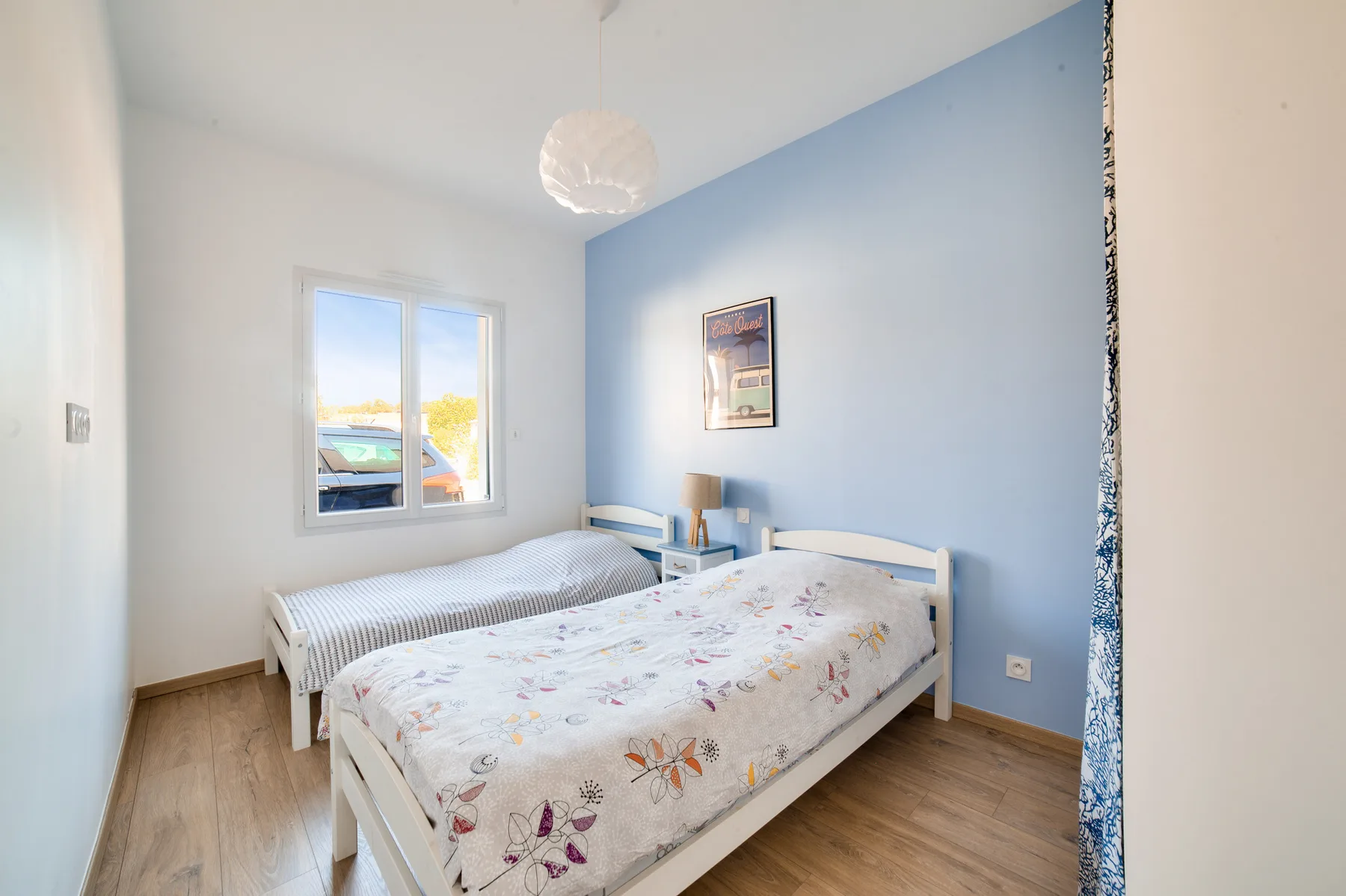 A bedroom with two beds, a window, and a light blue accent wall.