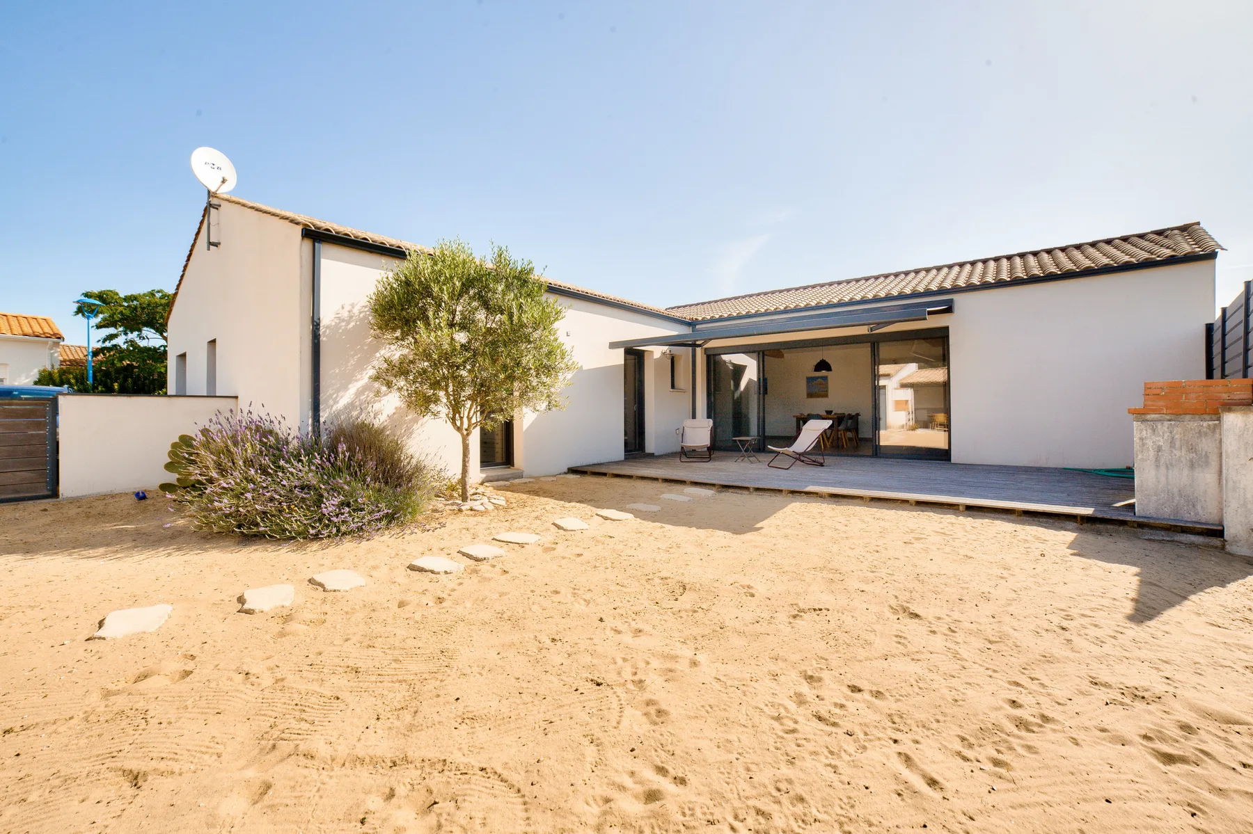 A modern house opens onto a sandy courtyard with a small patio.