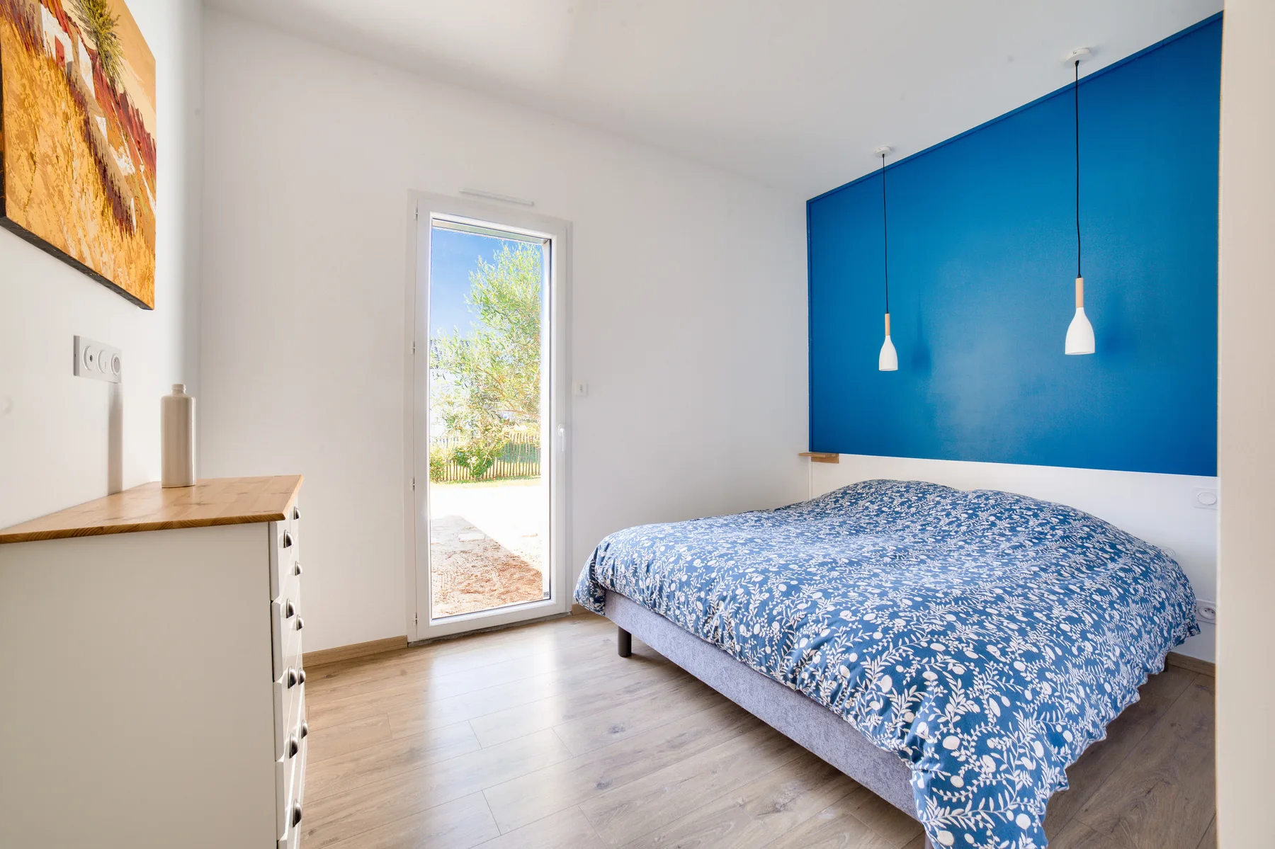 A bedroom with a bed beneath a bright blue wall and a narrow window.