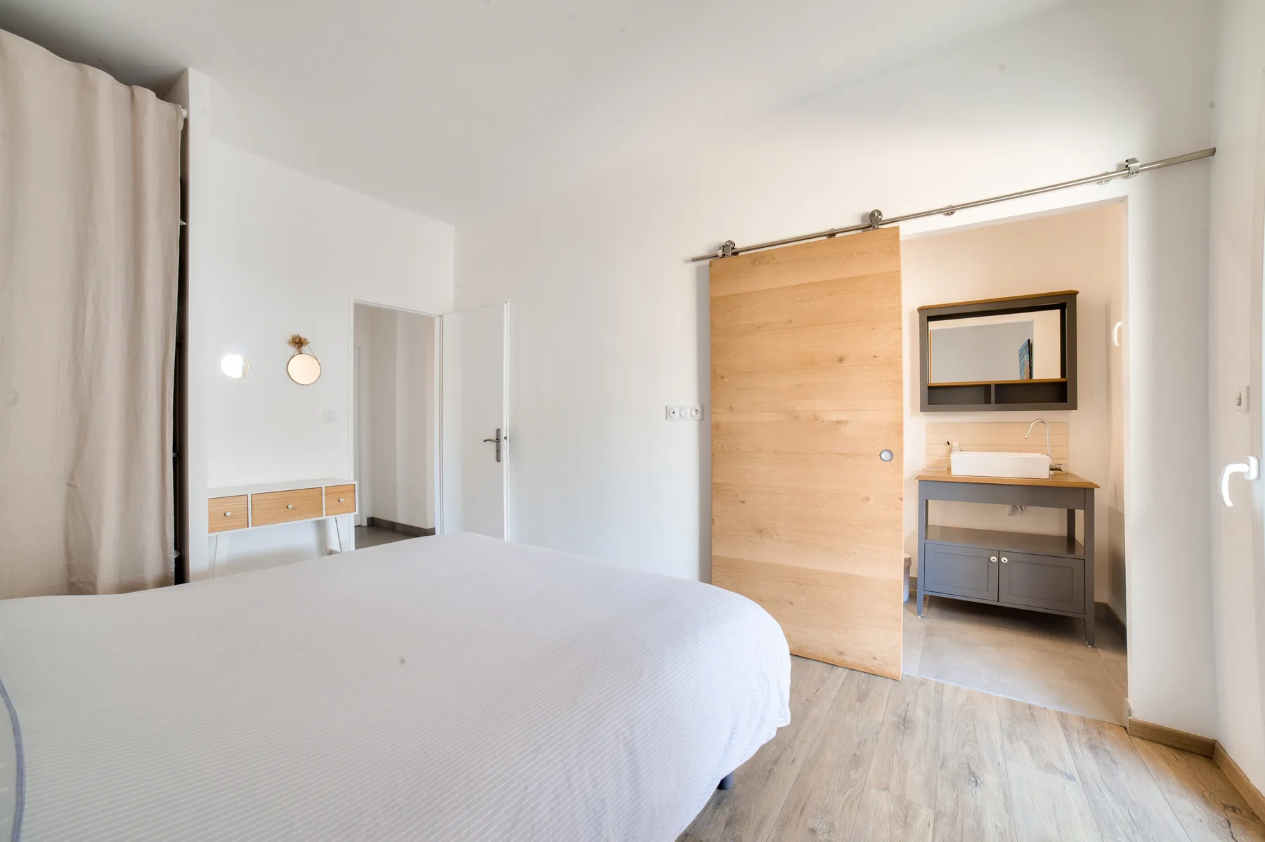 A bright bedroom with a bed and a sliding wooden door.