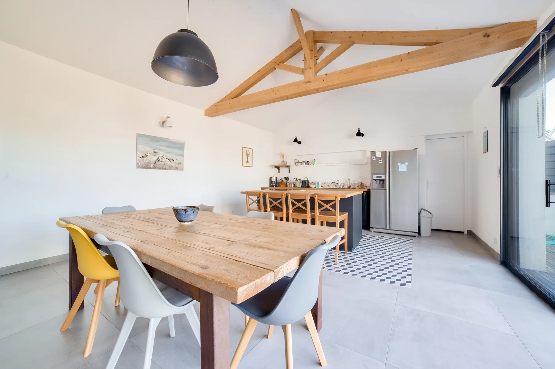 A bright dining area with a long wooden table and exposed ceiling beams.