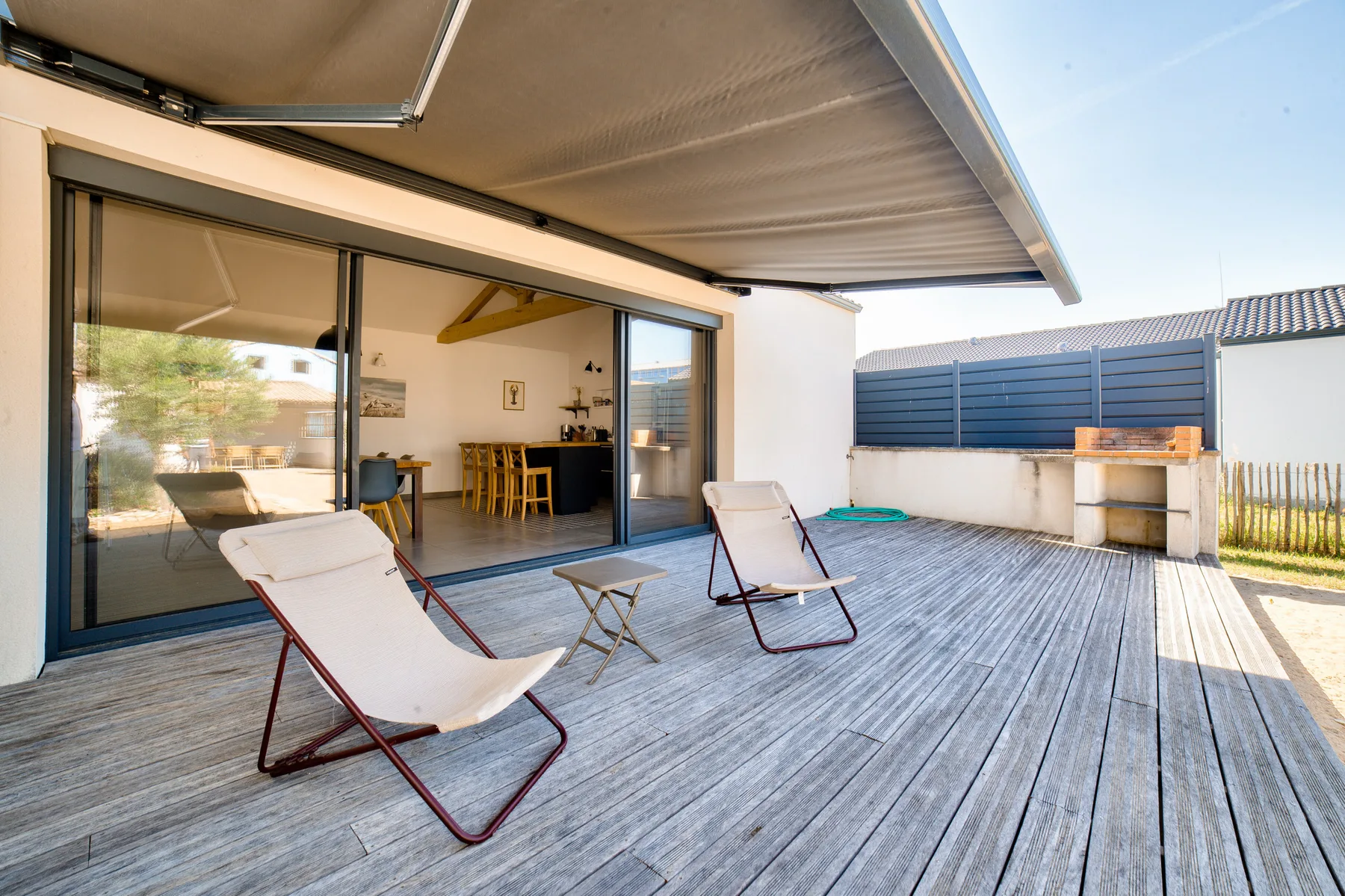 A covered outdoor deck has reclining seating beside open sliding glass doors.