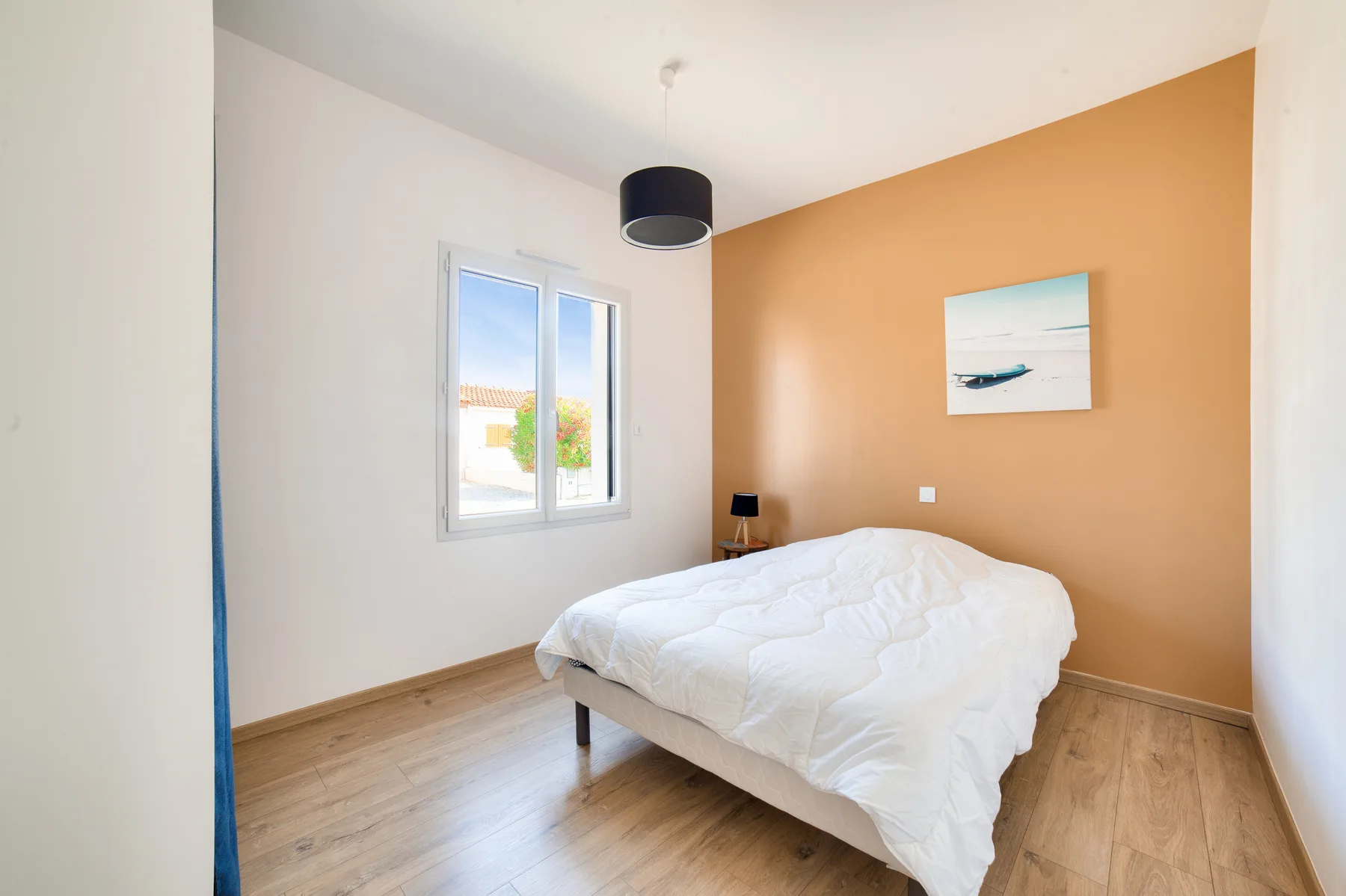 A bedroom with a white bed beside a window and an orange accent wall.