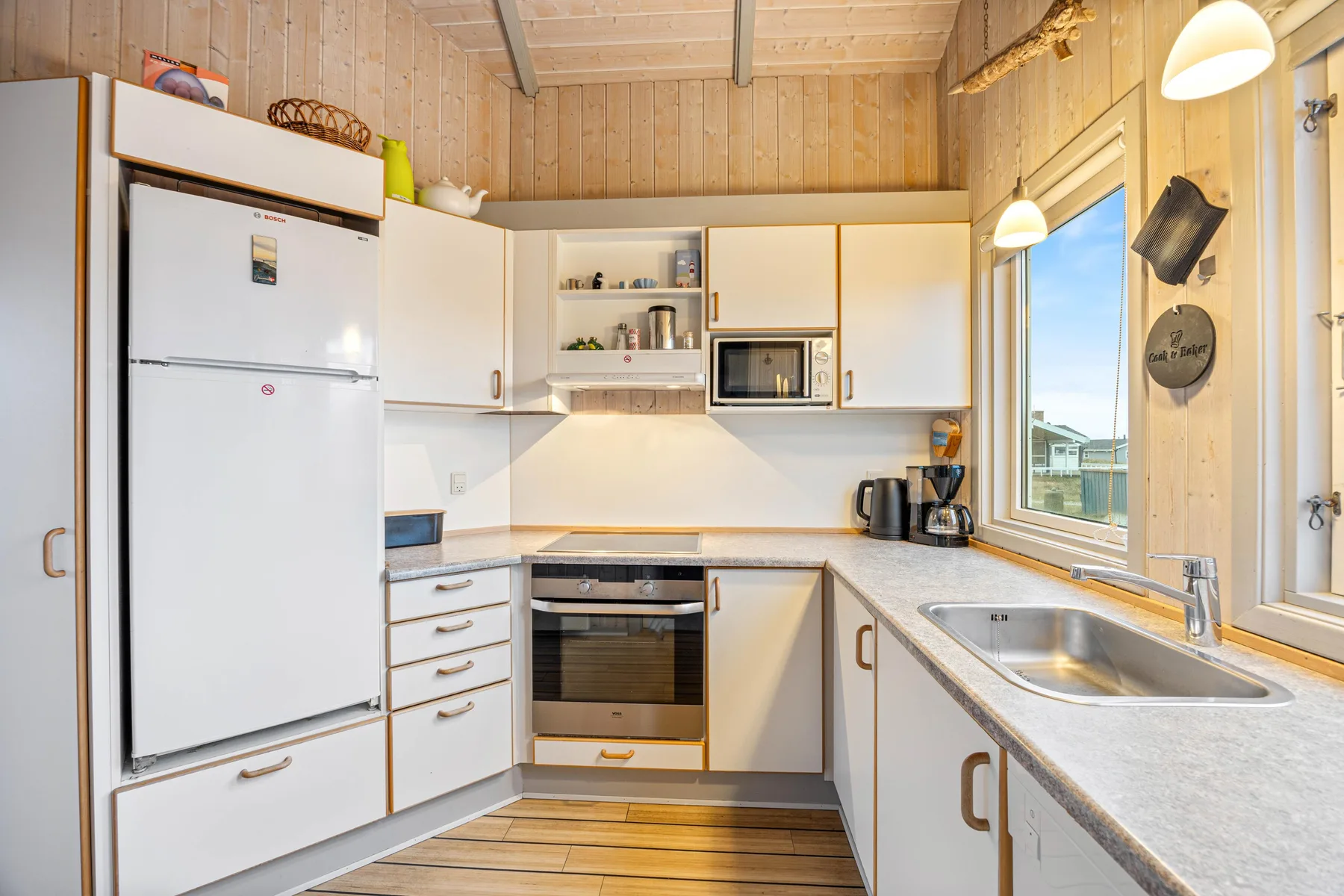 Una cocina compacta con gabinetes blancos, un refrigerador y un fregadero bajo una ventana.