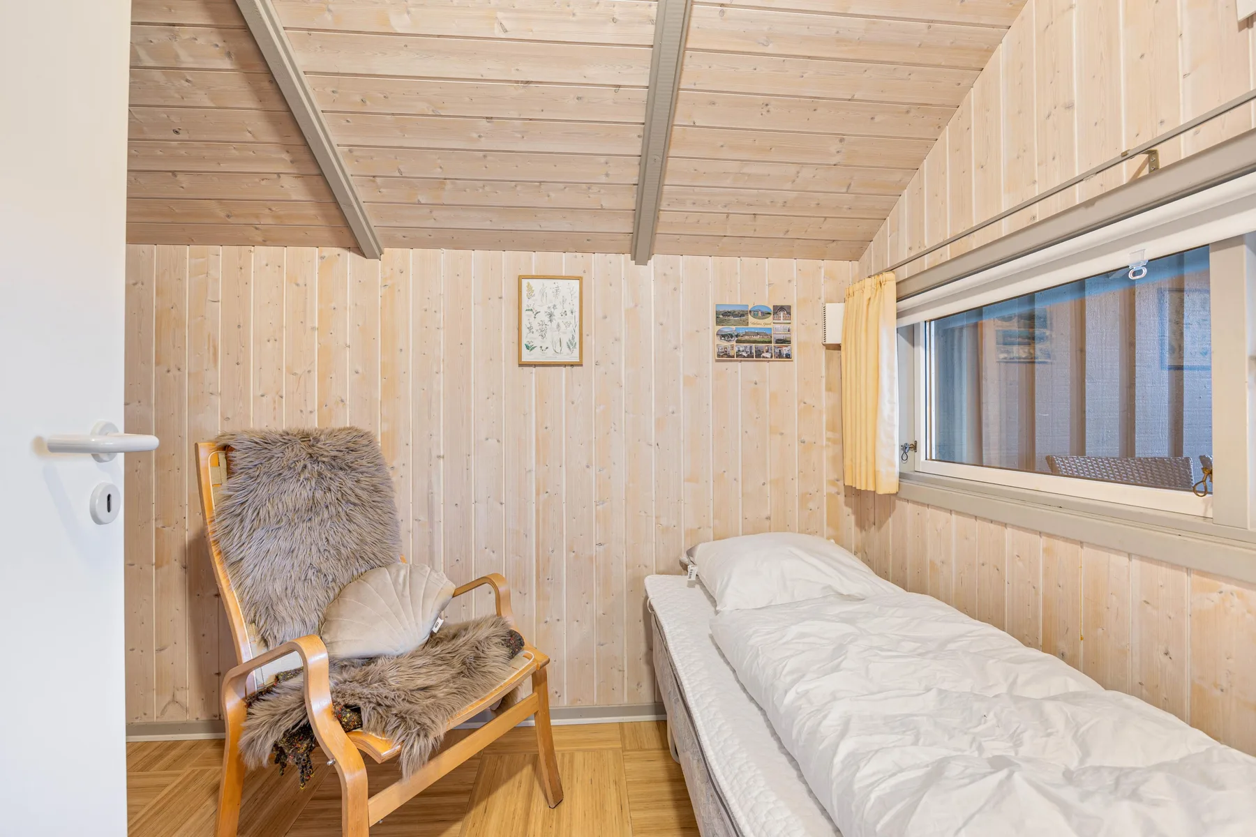 Un dormitorio revestido de madera con una cama individual y un sillón acolchado.