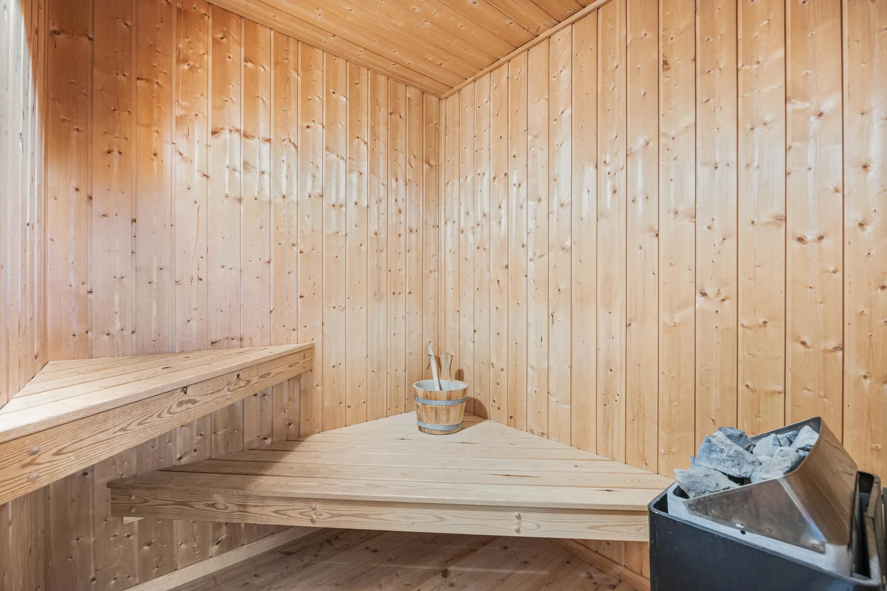 Una sauna de madera con bancos escalonados y un calentador en una esquina.