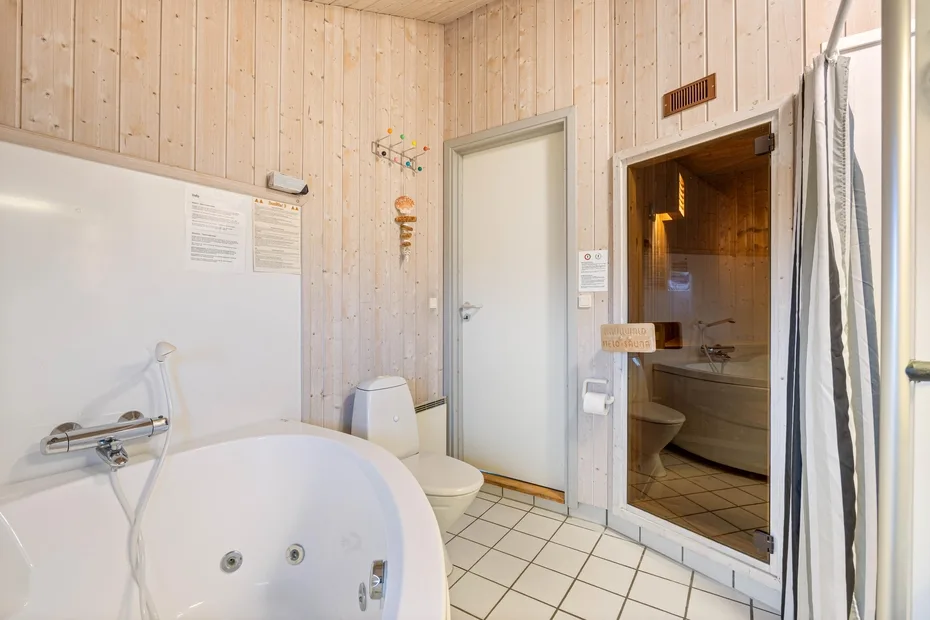 Un baño con suelo de baldosas, bañera, inodoro y zona de ducha acristalada.