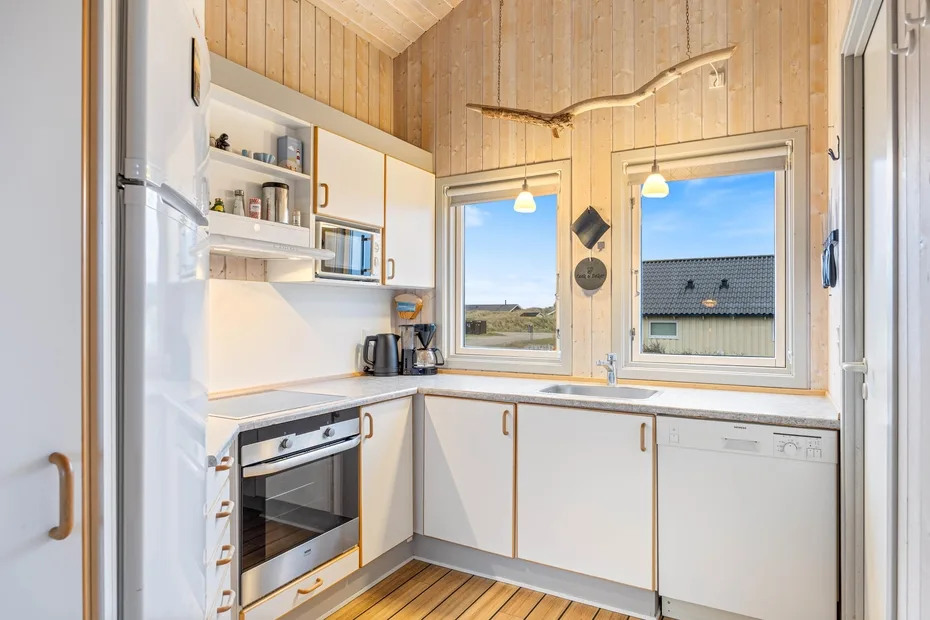 Una cocina compacta con armarios blancos, una encimera y ventanas con vistas al exterior.