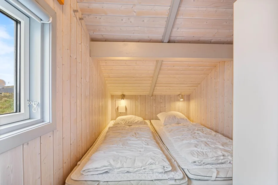 Un dormitorio compacto con dos camas individuales bajo un techo de madera inclinado.