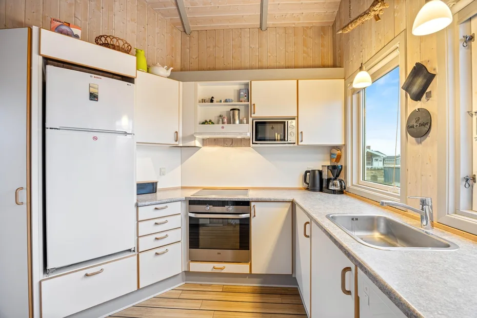 Una cocina compacta con gabinetes blancos, un refrigerador y un fregadero.