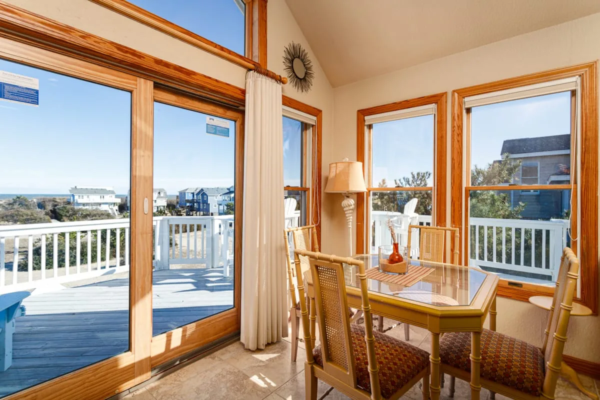 Un comedor luminoso con una mesa de vidrio junto a grandes ventanas con vistas a una terraza.