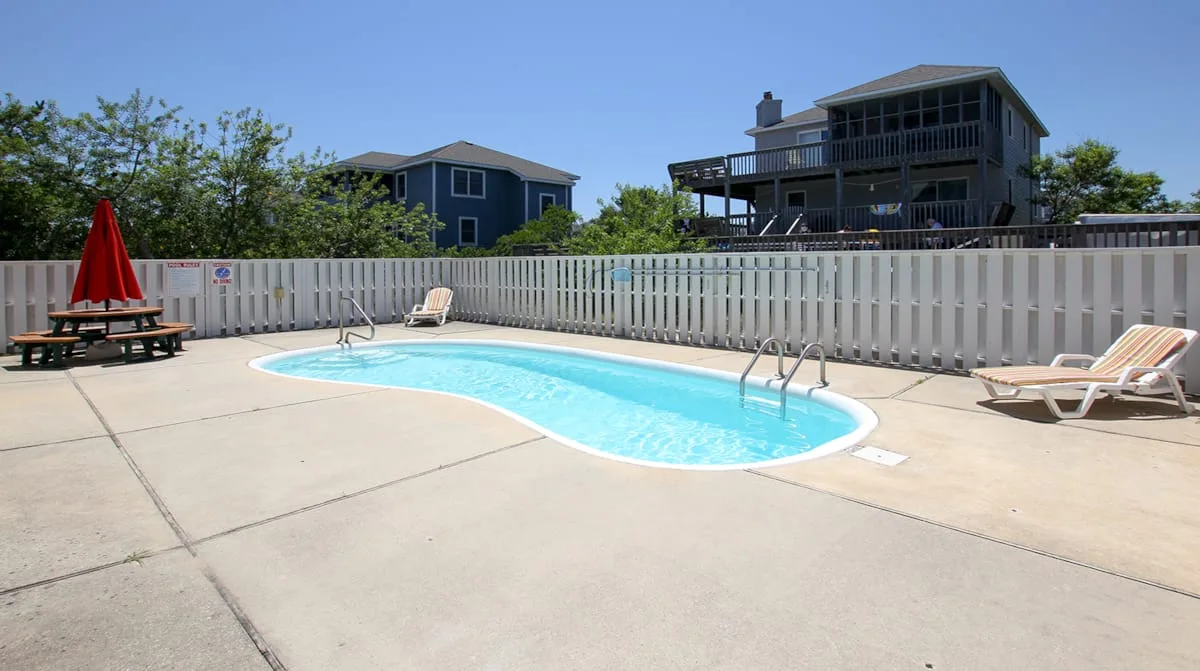 Una piscina al aire libre está junto a una cerca blanca y asientos de patio.