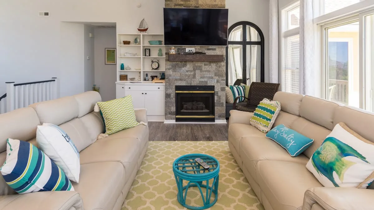 Una sala luminosa con sofás frente a una chimenea de piedra y un televisor.