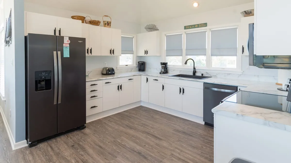 Una cocina luminosa con gabinetes blancos, electrodomésticos oscuros y una amplia encimera.