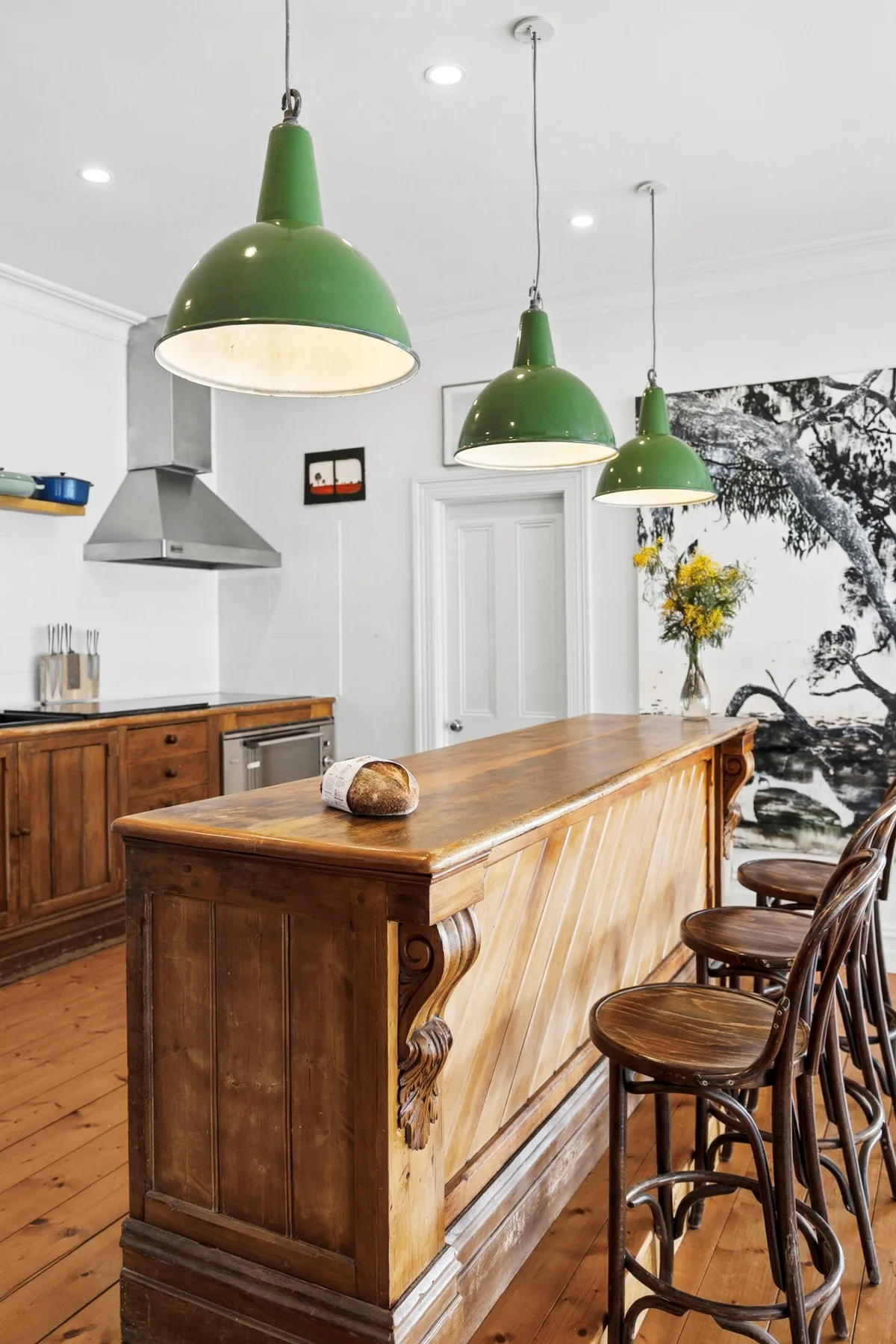 Una cocina con una isla de madera, taburetes y lámparas colgantes verdes.