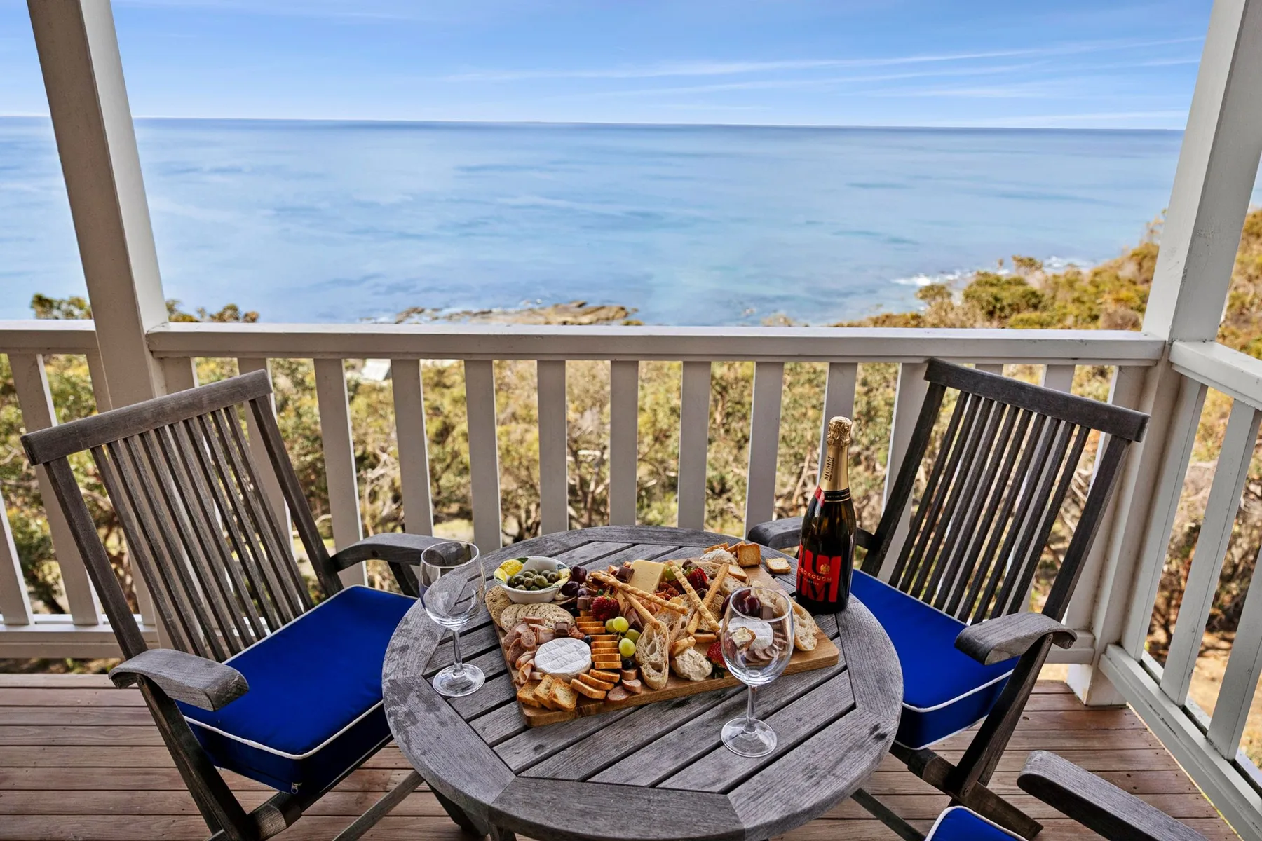 Una zona de comedor en el balcón da al mar, con una mesa servida con comida y bebidas.