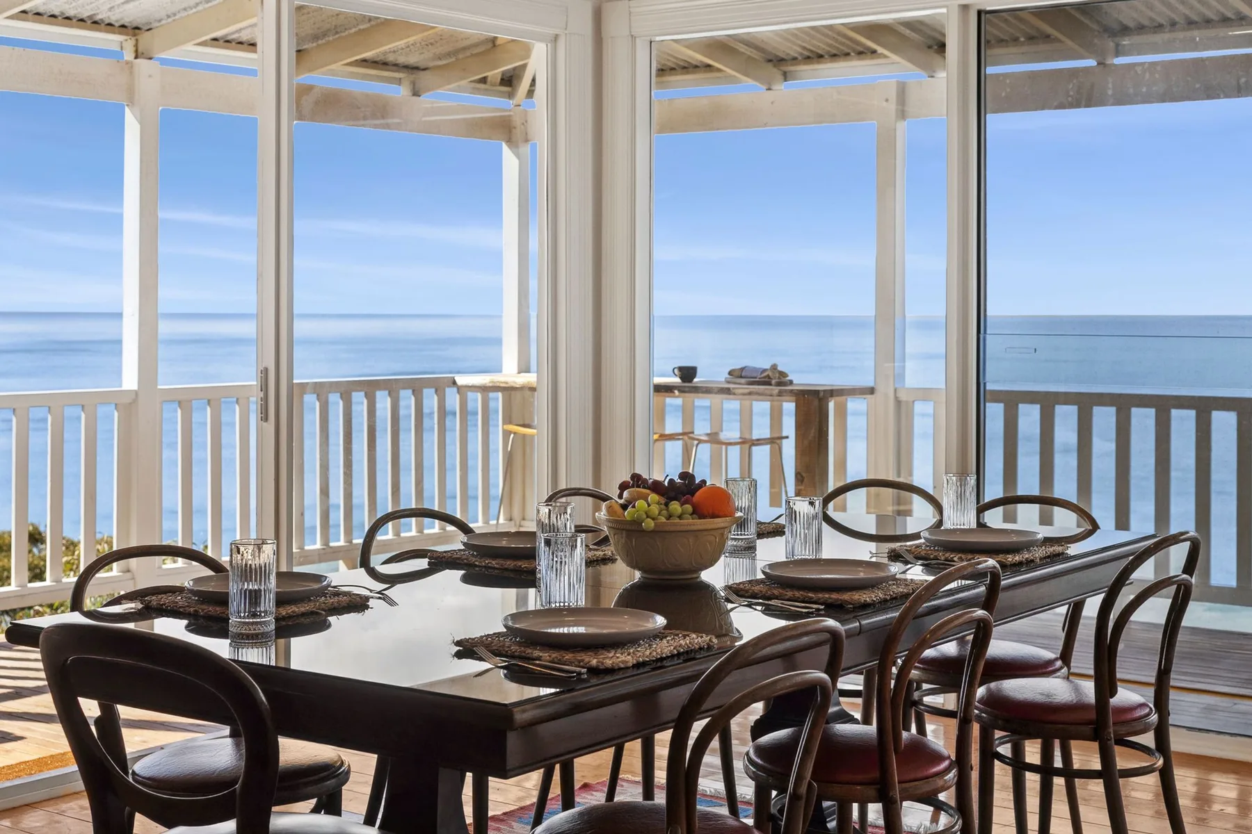 Comedor con la mesa puesta junto a grandes ventanales con vistas al océano.