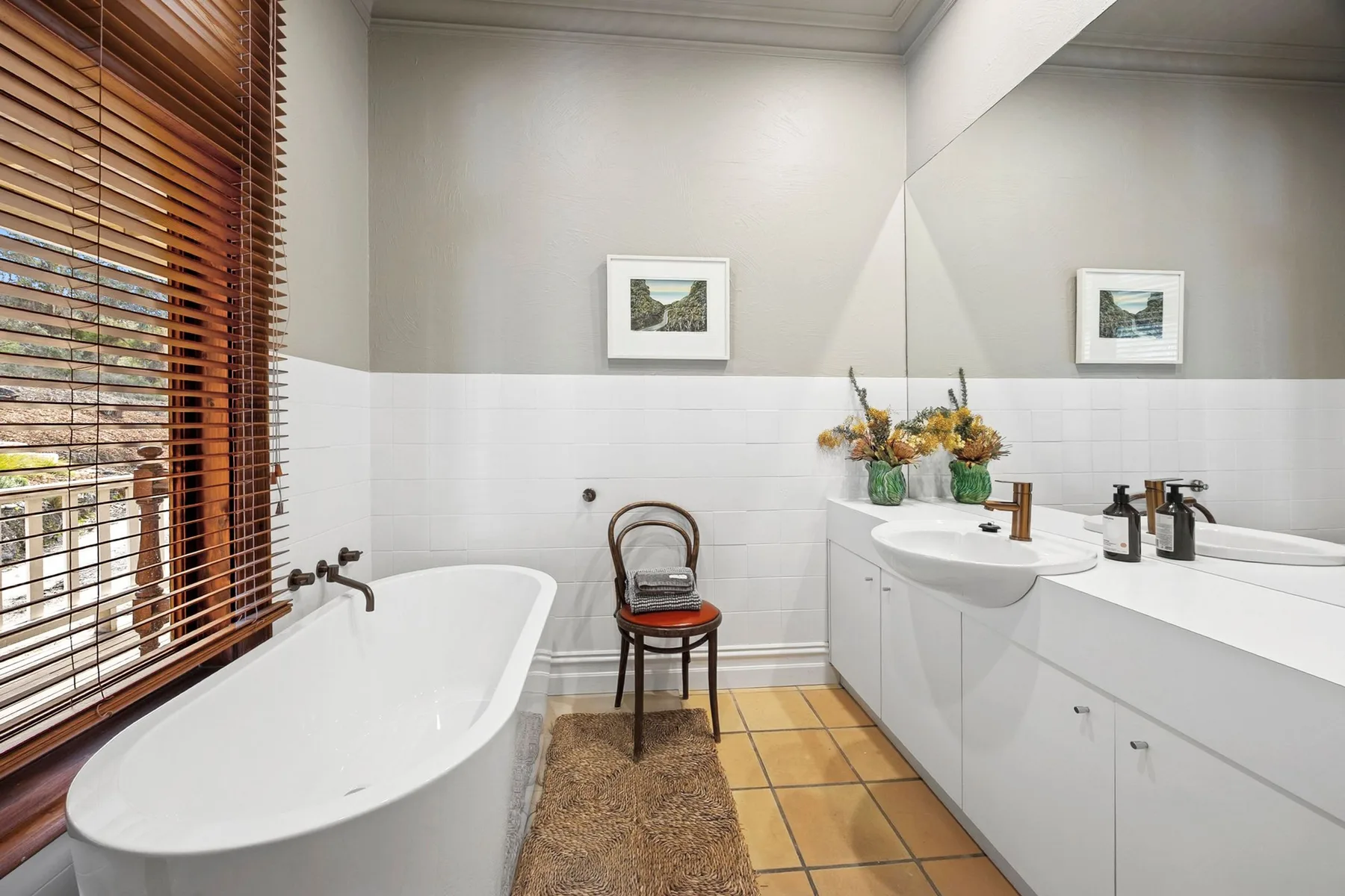 Un baño con bañera, lavabo y persianas de madera en la ventana.