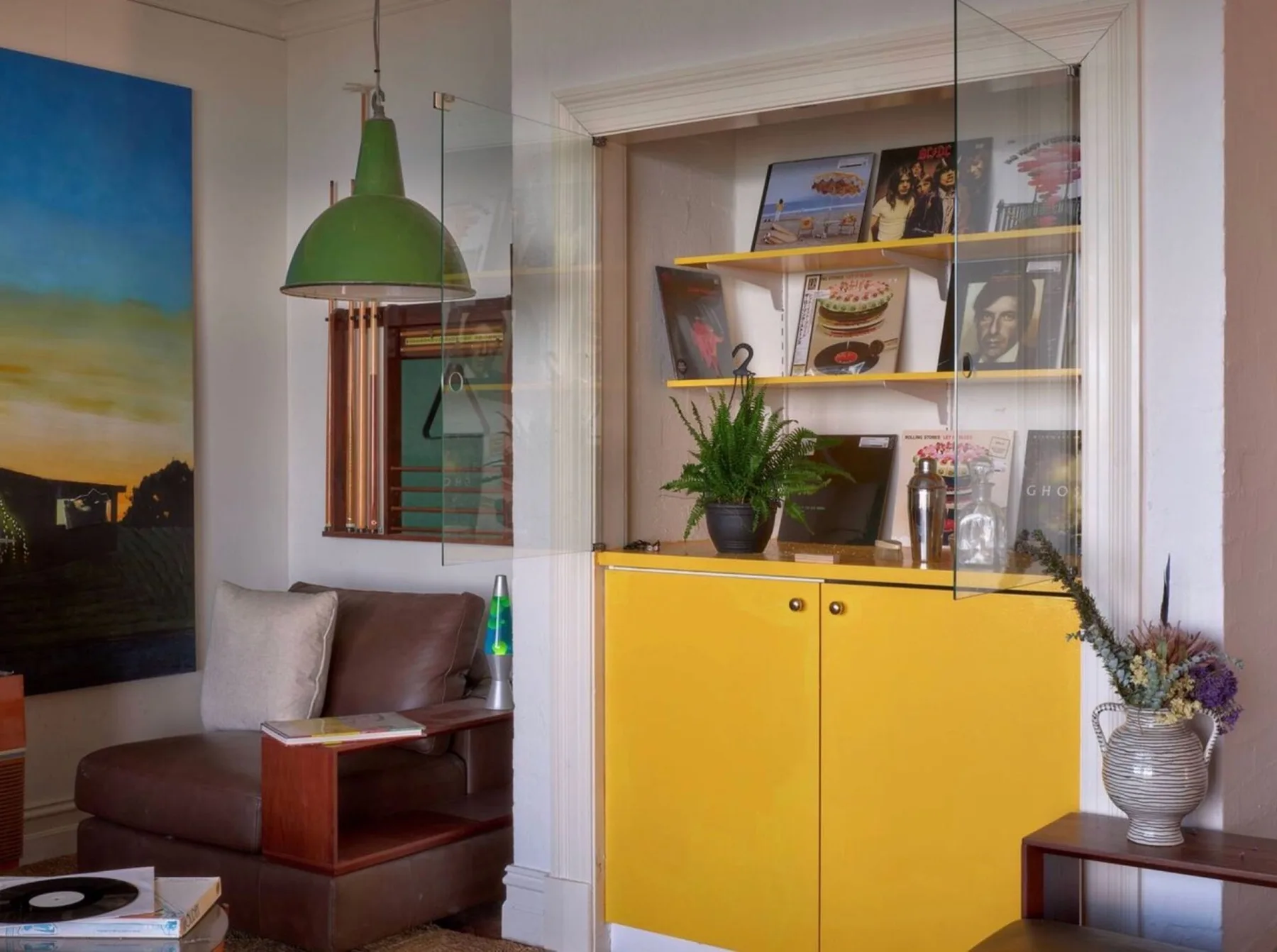 Una sala de estar con un mueble amarillo que exhibe libros y obras enmarcadas.