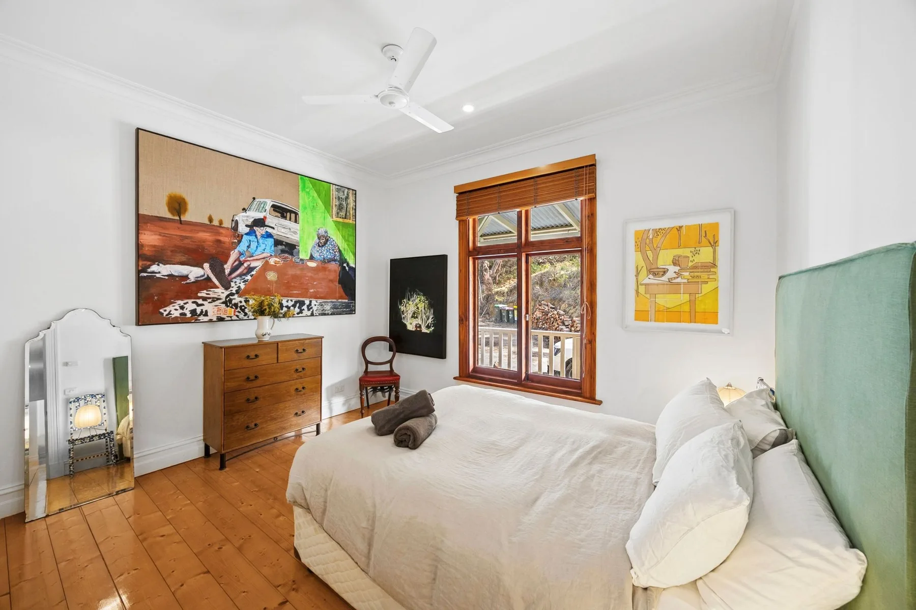 Un dormitorio luminoso con una cama grande, muebles de madera y obras de arte coloridas.