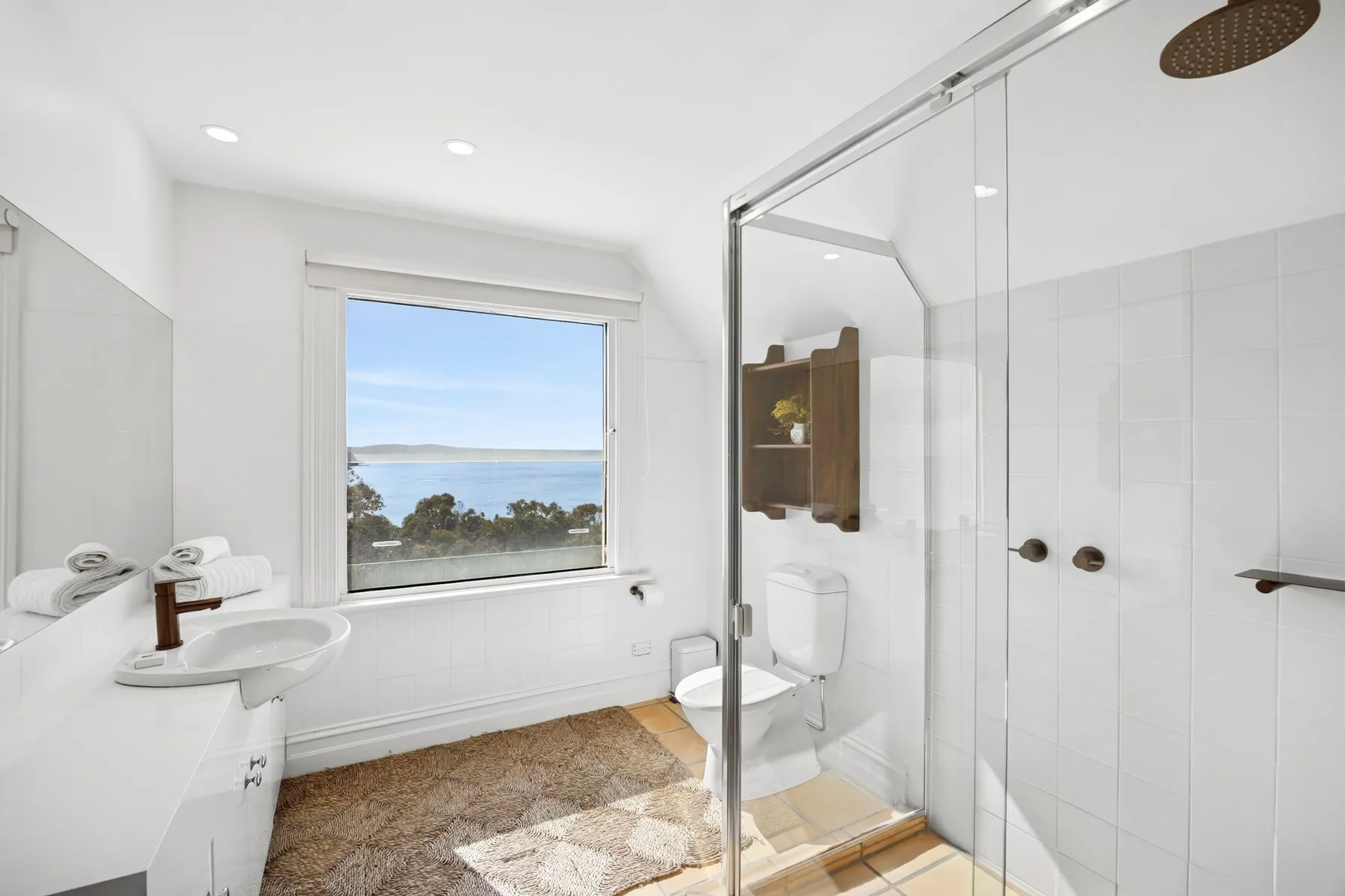 Un baño luminoso con una ventana con vistas al mar y una ducha de cristal.
