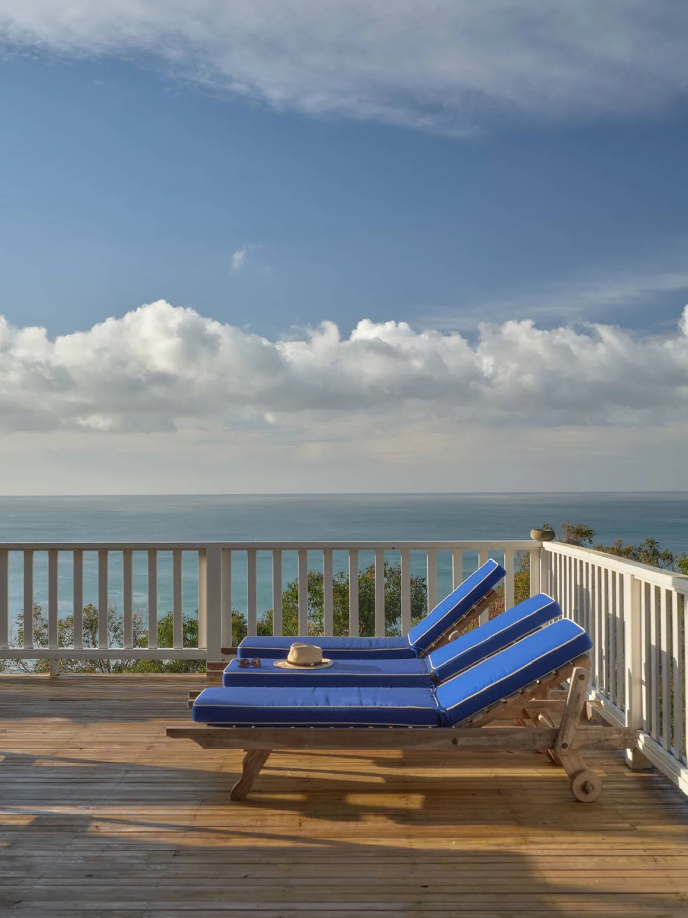 Una terraza de madera mira al océano, con asientos azules junto a una barandilla.