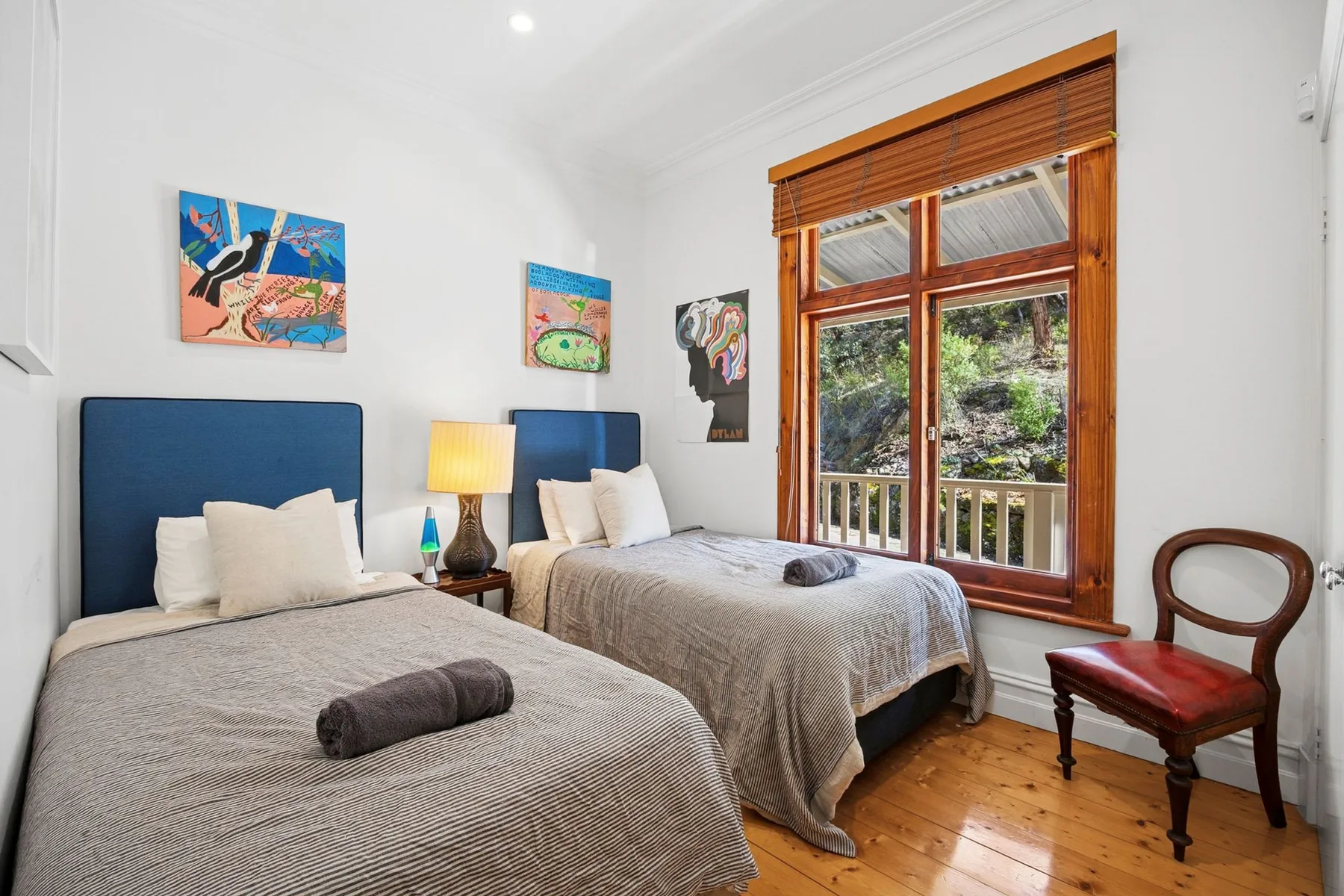 Un dormitorio luminoso con dos camas, arte colorido en la pared y una ventana grande.