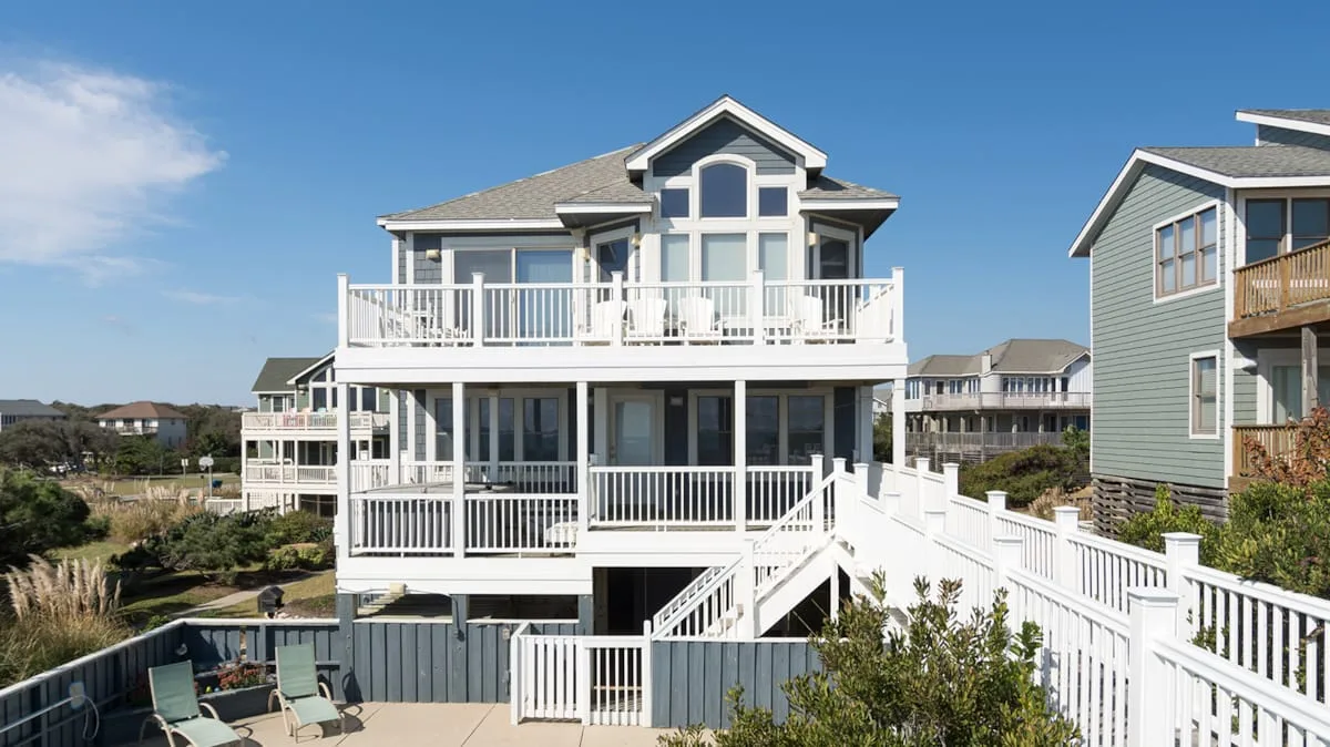 A large coastal-style house has white decks and exterior stairs.