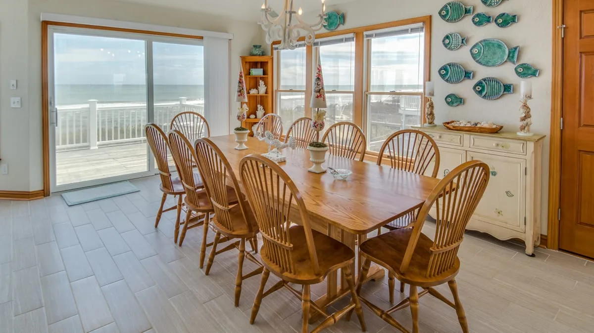Un comedor con una mesa de madera y grandes ventanas con vista al agua.