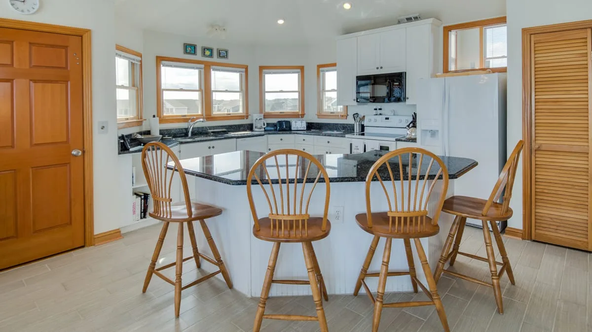 A bright kitchen with a counter and wooden seating.