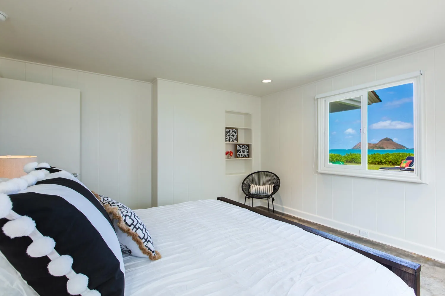 Un dormitorio con una cama y una gran ventana con vistas a un paisaje costero verde.