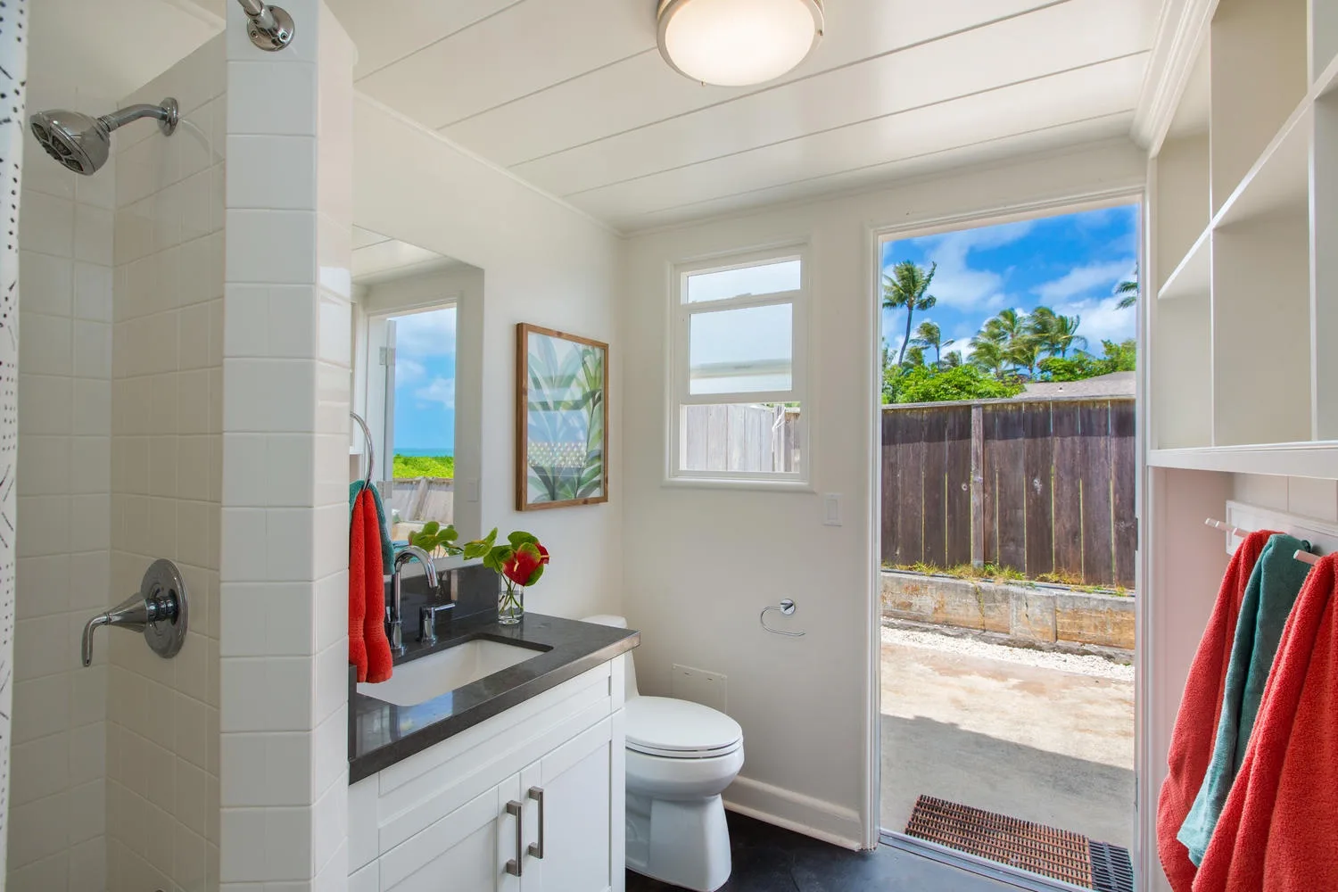 Un baño luminoso con lavabo, inodoro y una ventana con vista a un patio cercado.