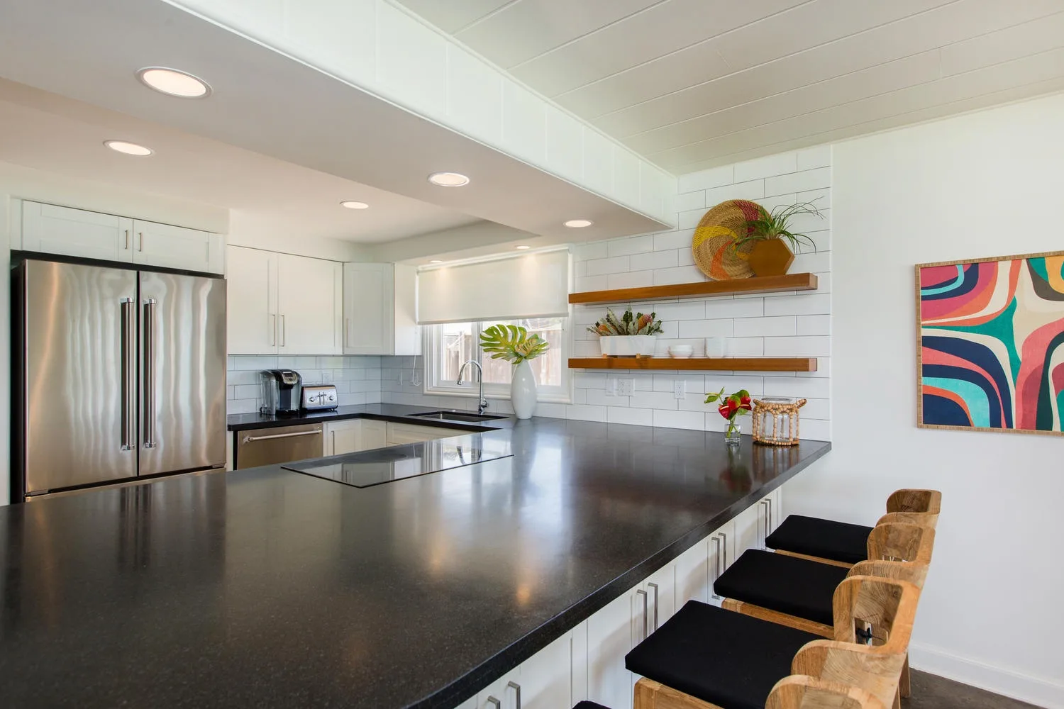 Una cocina luminosa con una gran isla, refrigerador de acero inoxidable y estantes abiertos.