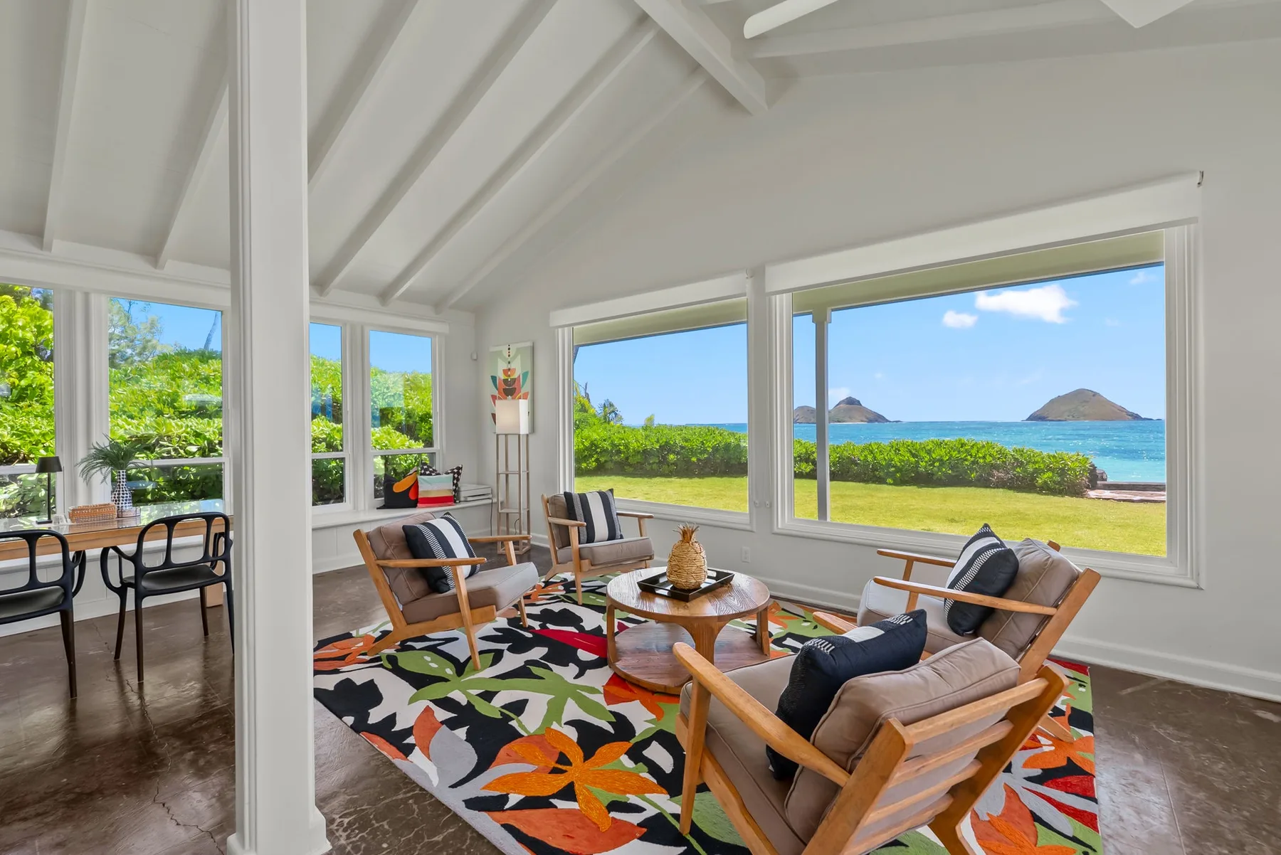 Una sala luminosa con asientos alrededor de una mesa baja y grandes ventanas con vistas al mar.