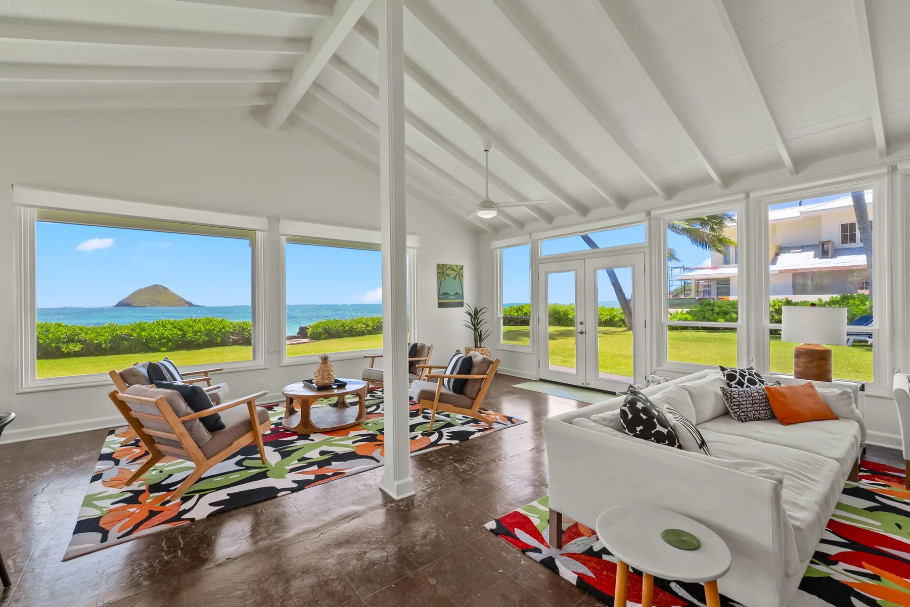 Una luminosa sala de estar con asientos, grandes ventanas y vistas al mar y la vegetación.