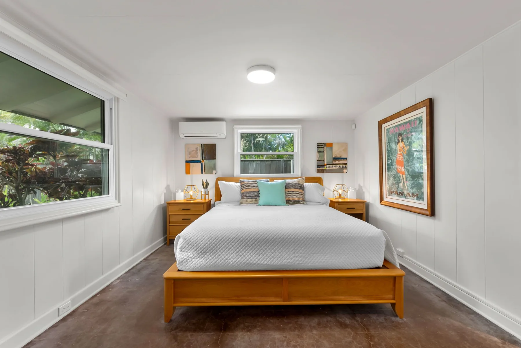Un dormitorio luminoso con una cama bien arreglada y una obra enmarcada.
