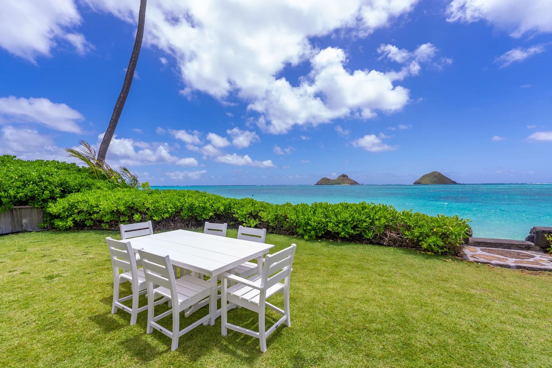 Una mesa de comedor al aire libre con asientos da a un césped, aguas turquesas e islas lejanas.