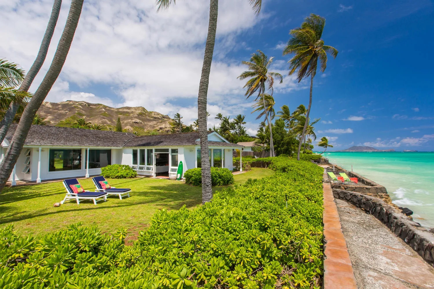 Una casa junto a la playa está rodeada de césped, palmeras y aguas turquesas.