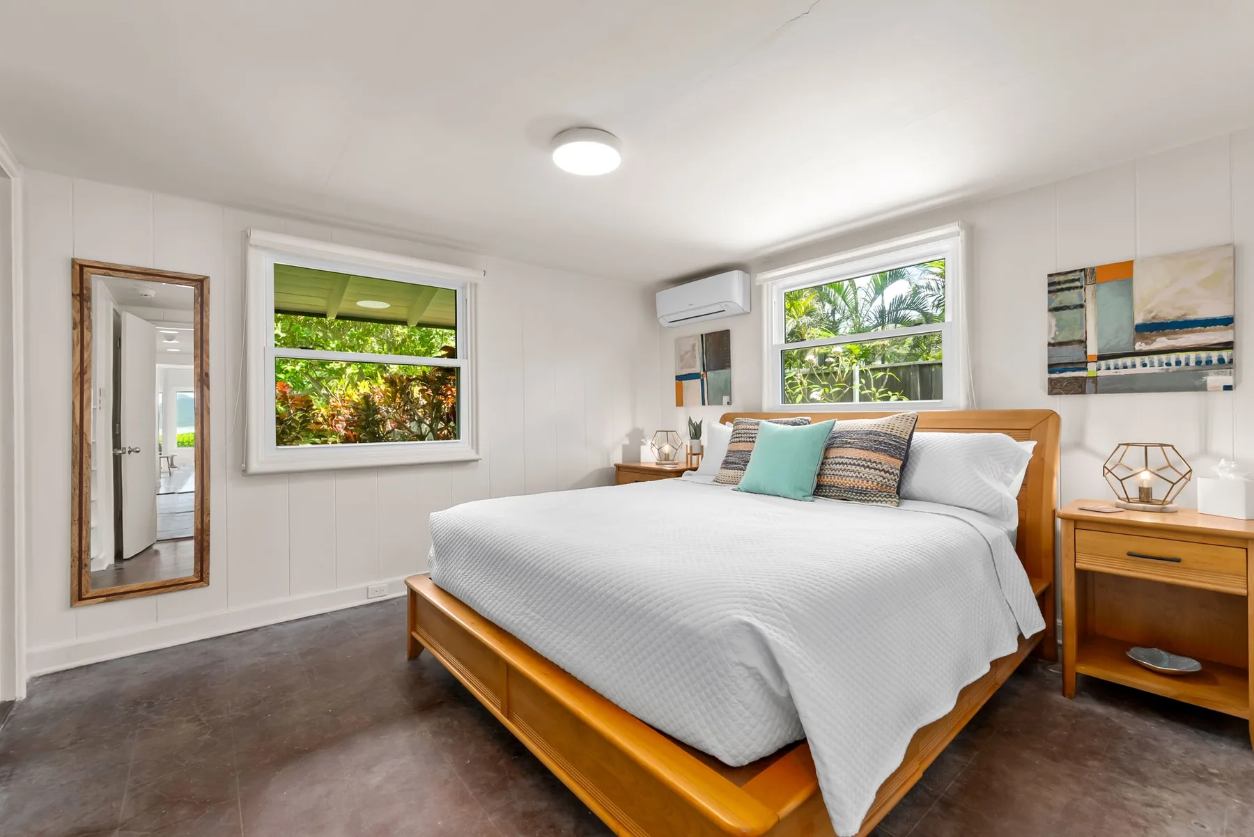 Un dormitorio luminoso con una cama grande, mesas de noche y ventanas con vistas a la vegetación.