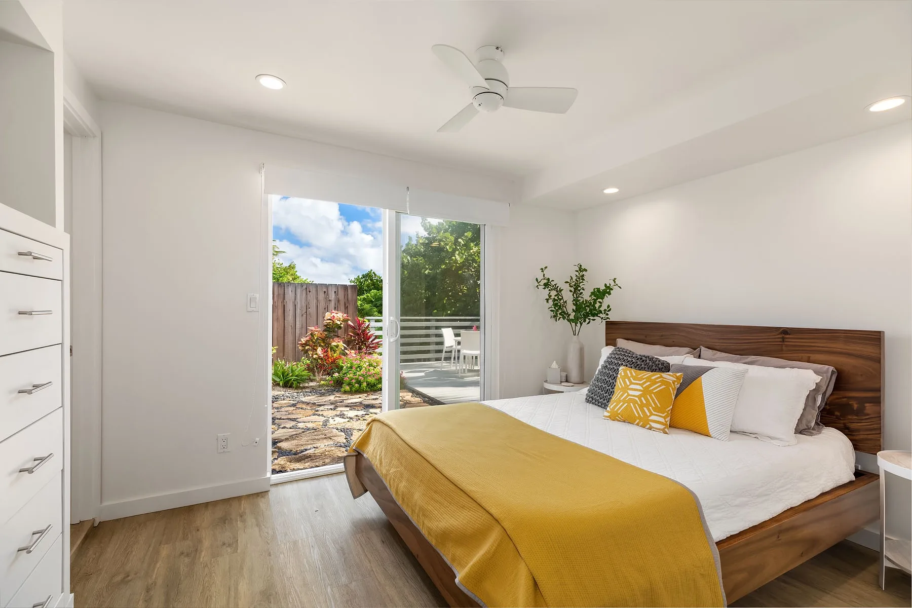 Un dormitorio luminoso con una cama de madera frente a puertas corredizas de vidrio hacia un jardín.