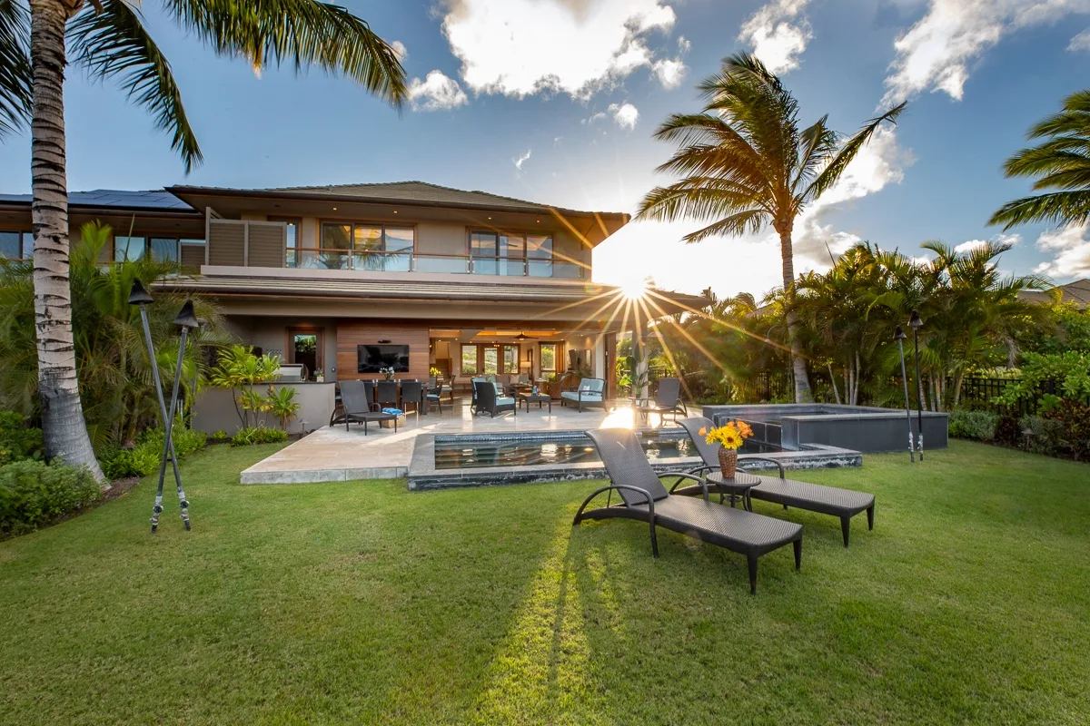 Una casa moderna da a un césped, un patio y una piscina al atardecer.
