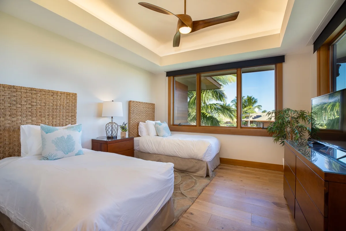 Un dormitorio luminoso con dos camas y una amplia ventana con palmeras a la vista.