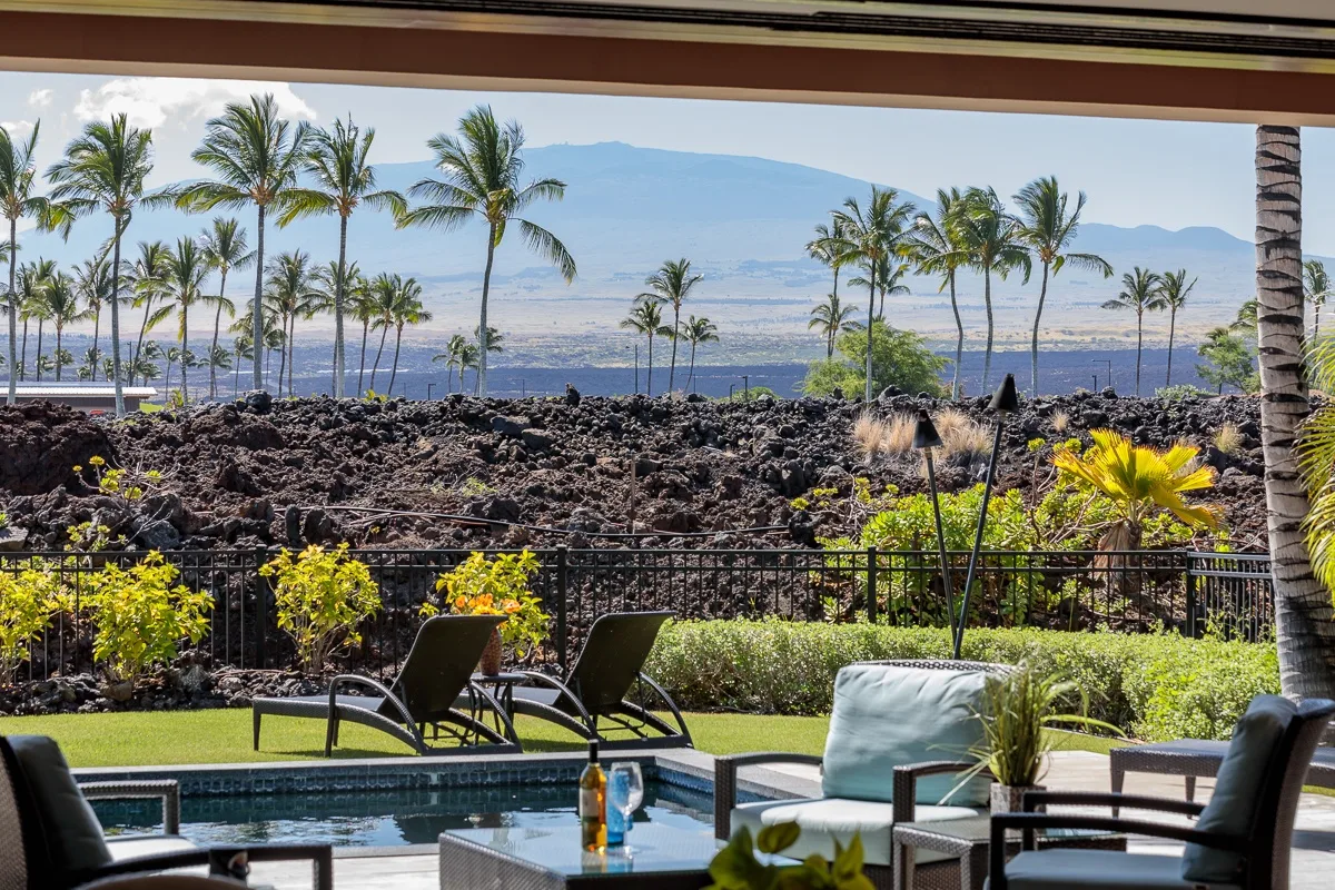 Un patio da a una piscina, rocas de lava, palmeras y el océano.