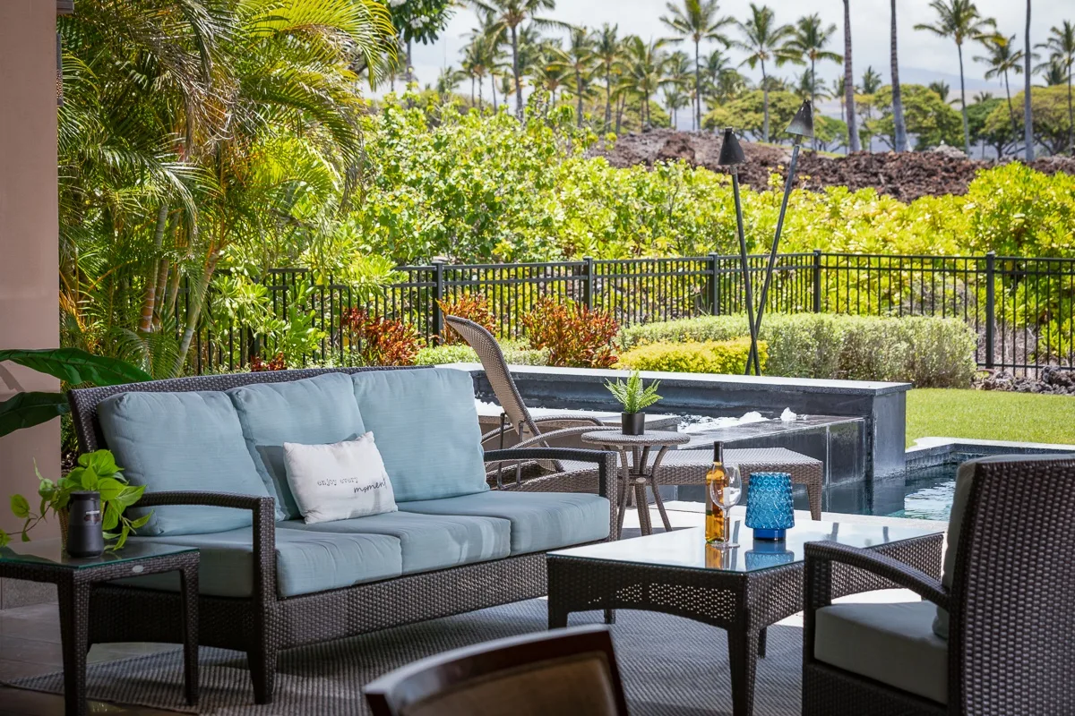 Un patio al aire libre con asientos acolchados y una mesa junto a una piscina.