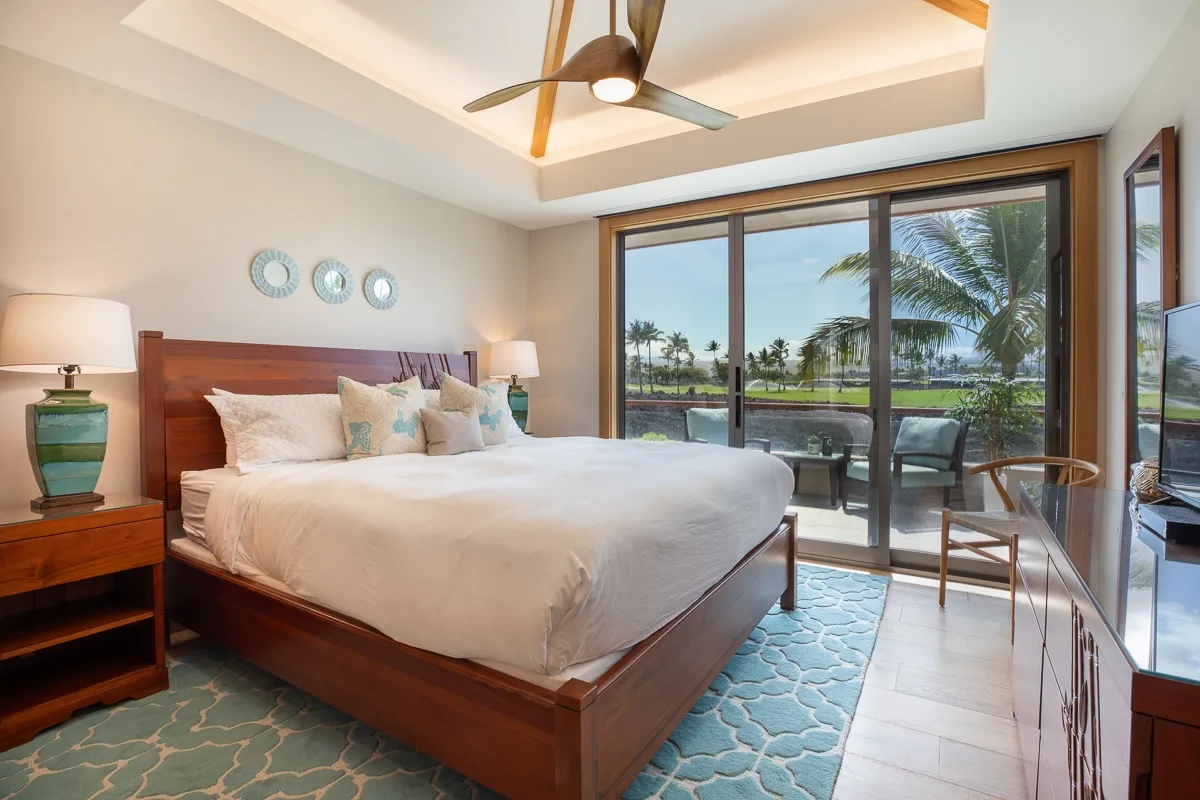 Un dormitorio con una cama grande junto a puertas corredizas de vidrio con vista a palmeras.
