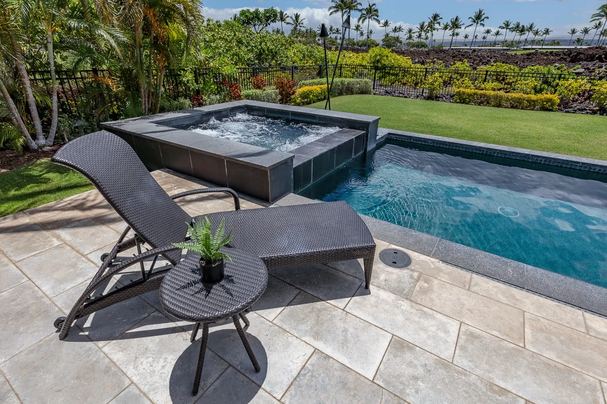 Una piscina exterior y un jacuzzi elevado junto a un patio pavimentado con asientos.