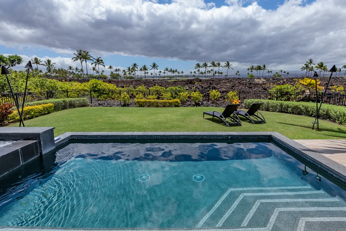 Una piscina al aire libre da a un césped ajardinado y campos bordeados de palmeras bajo un cielo nublado.