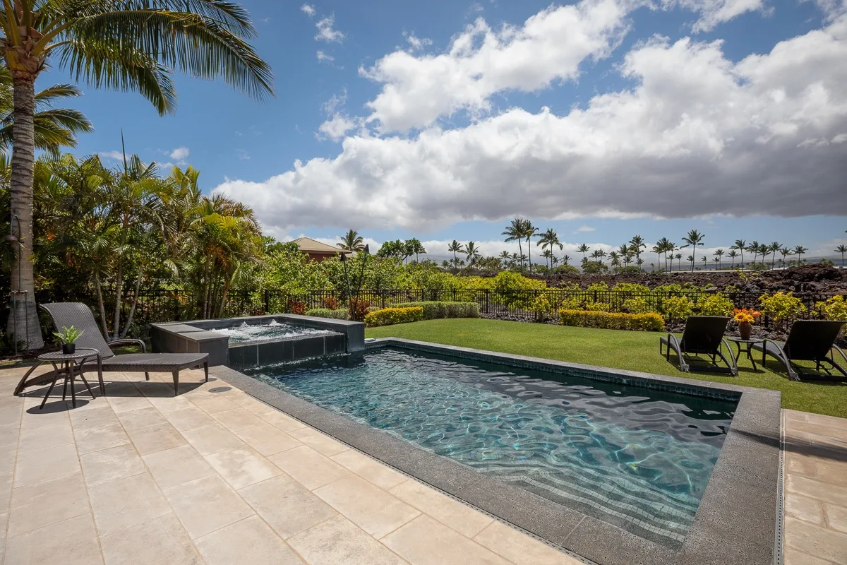 Una piscina exterior está junto a un patio de baldosas y jardines.