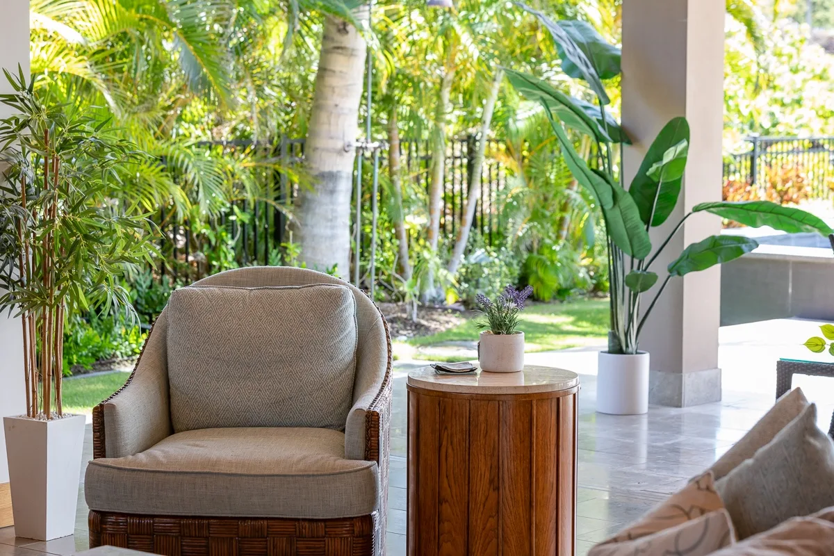 Una zona de estar cubierta se abre a un jardín frondoso, con un sillón y una mesa auxiliar.